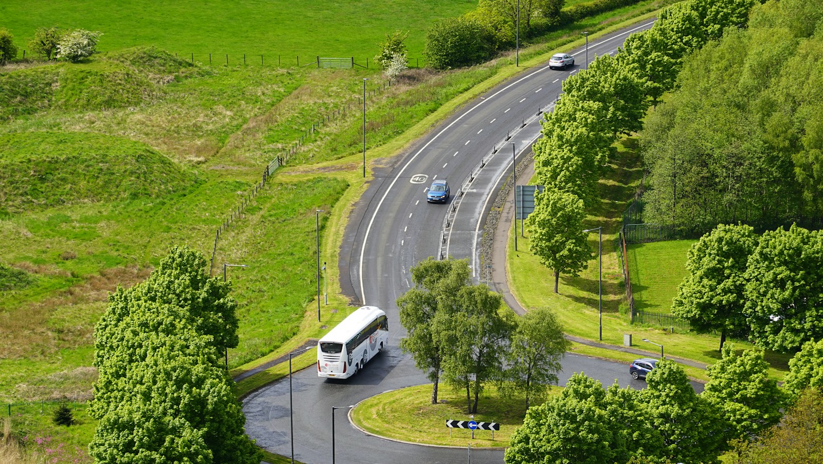 White coach bus driving on a road through green countryside