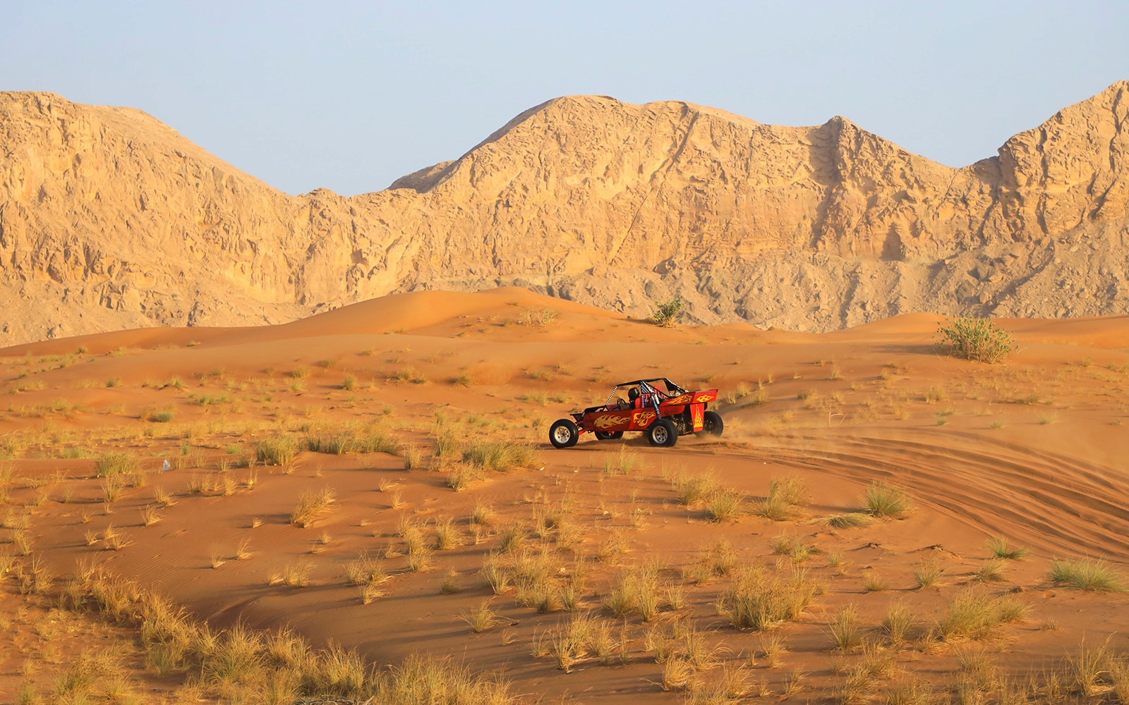 Kjøring med dune buggy på arabiske ørkendyner med steinete fjell i bakgrunnen.