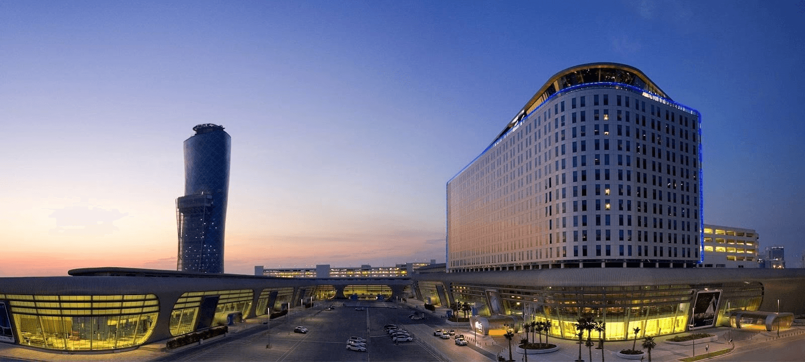 صورة خارجية تظهر أفق مدينة أبوظبي في الغروب، مع مبنى أدنيك بجوار فندق حياة ريجنسي.