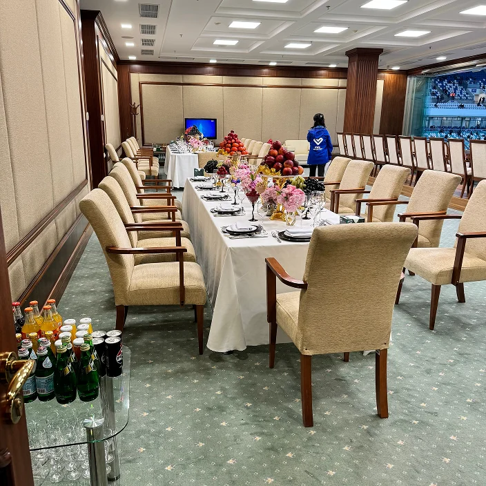 Formal dining room with a long white-covered table, floral and fruit centerpieces, cushioned chairs, and a beverage cart in an elegant, wood-paneled setting.