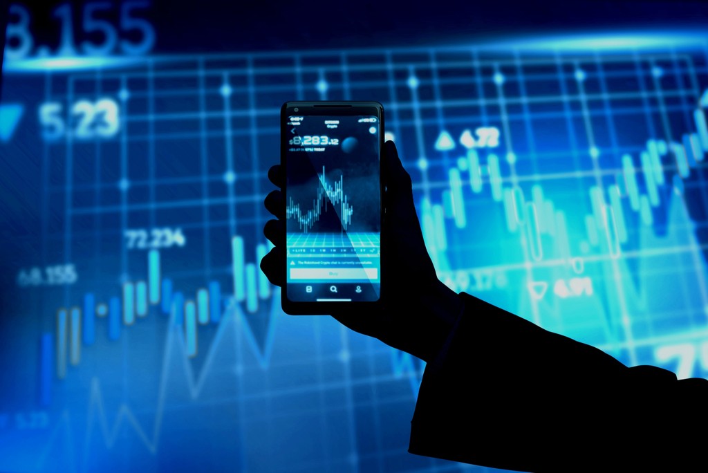 a person holding up a cell phone in front of a stock chart