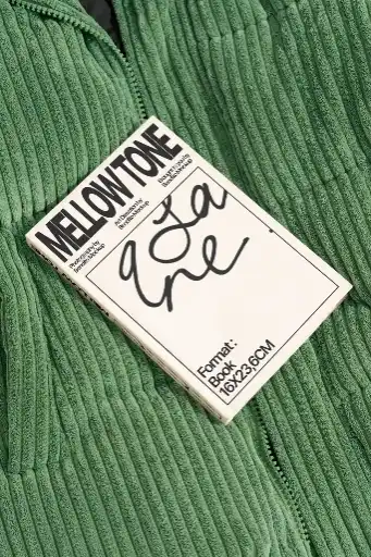 A vibrant book with a white cover and black border rests on green corduroy fabric. The book featuring bold typography and abstract design for a modern look.
