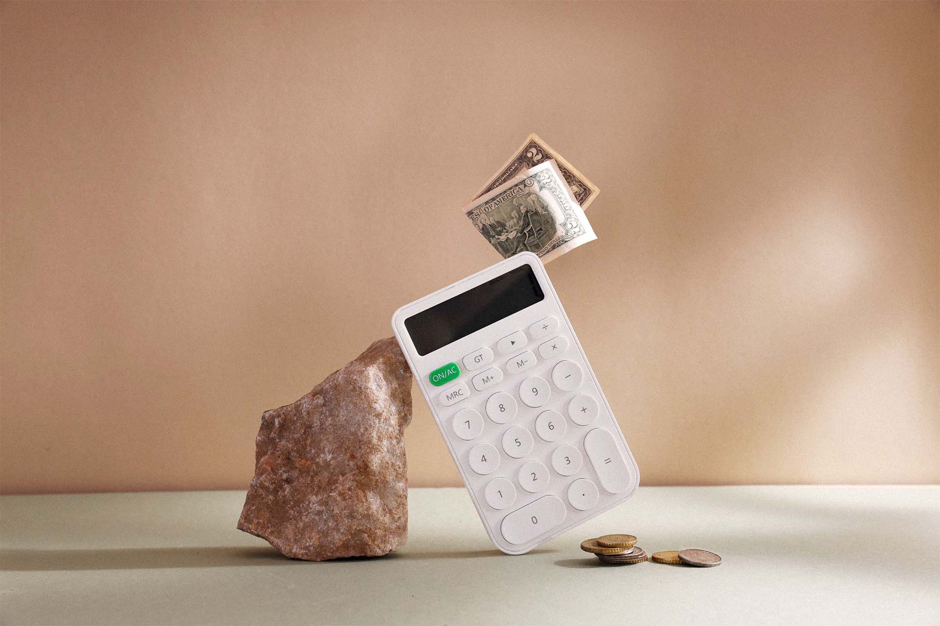 White calculator balanced on stone with dollar bills and coins