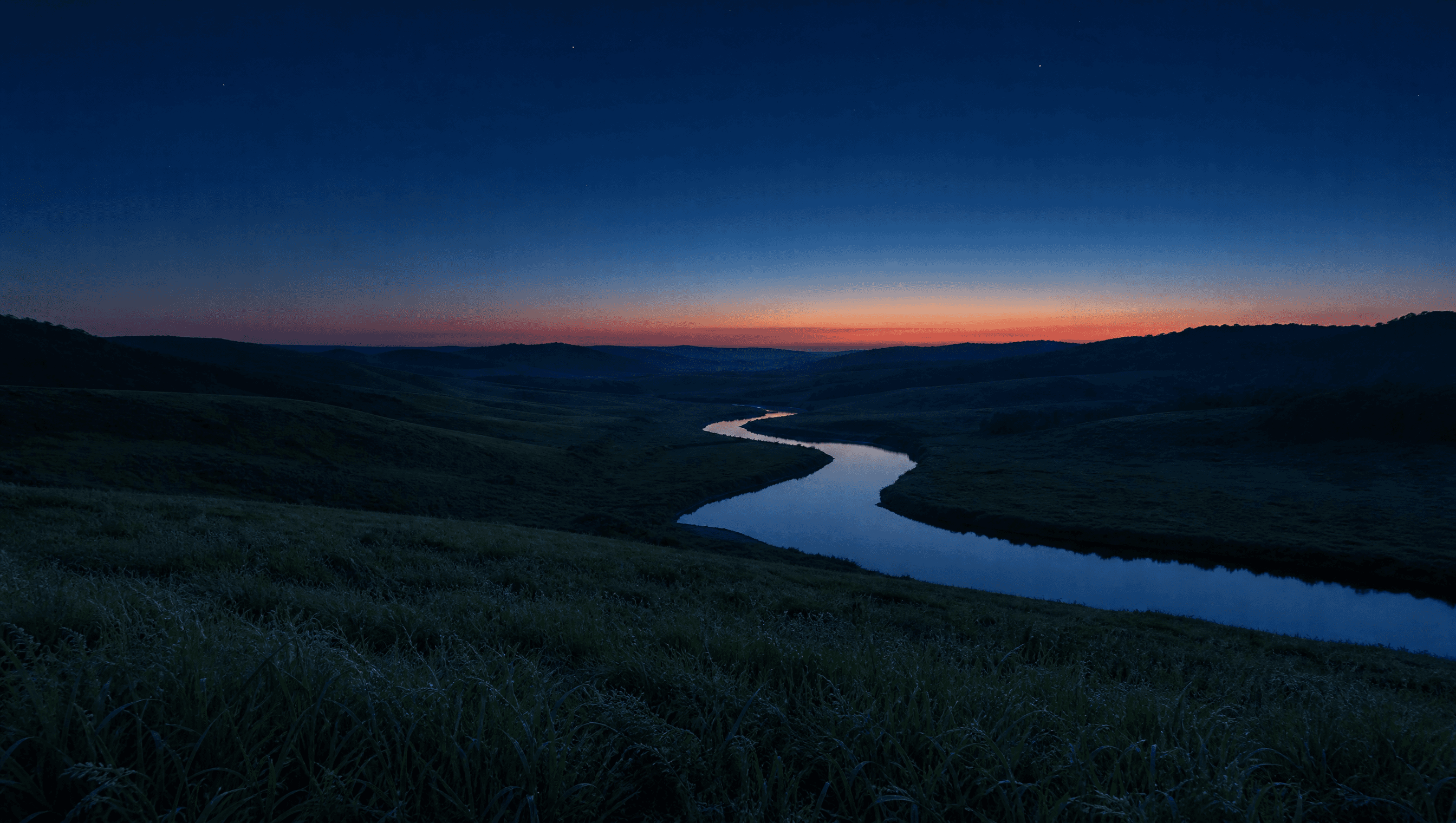 Mountain landscape at blue hour with a winding river through rolling hills