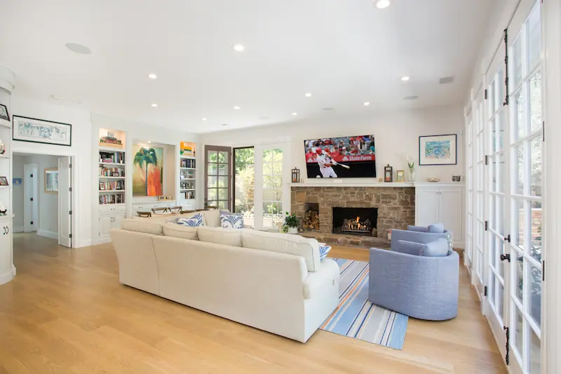 Wide view of bright and spacious living room with several french doors, white and blue furniture and stone clad fireplace from the Big Canyon Remodel project. Photo by Chris Darnall.
