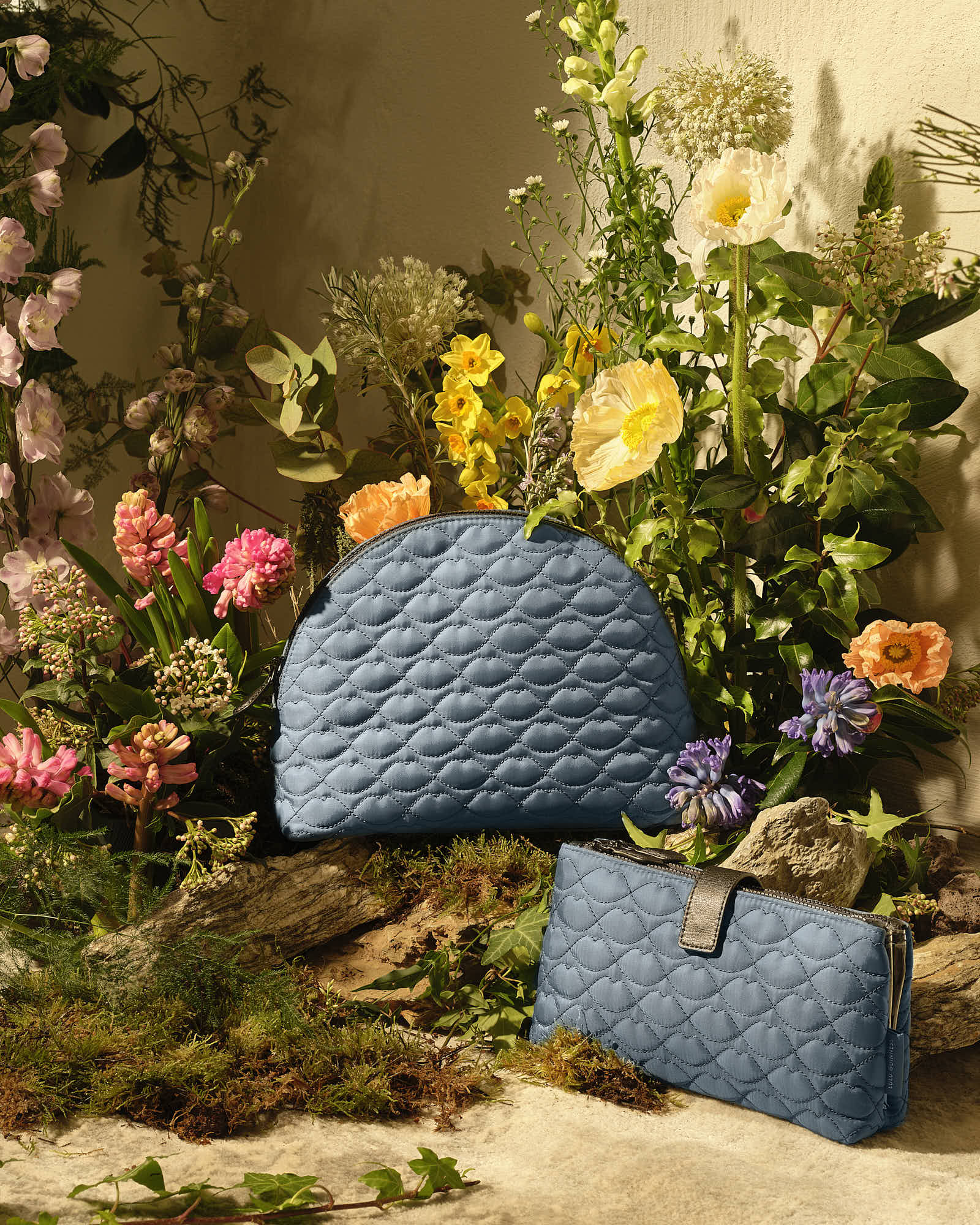 Blue quilted clutch and bag set amidst vibrant garden flowers and greenery.