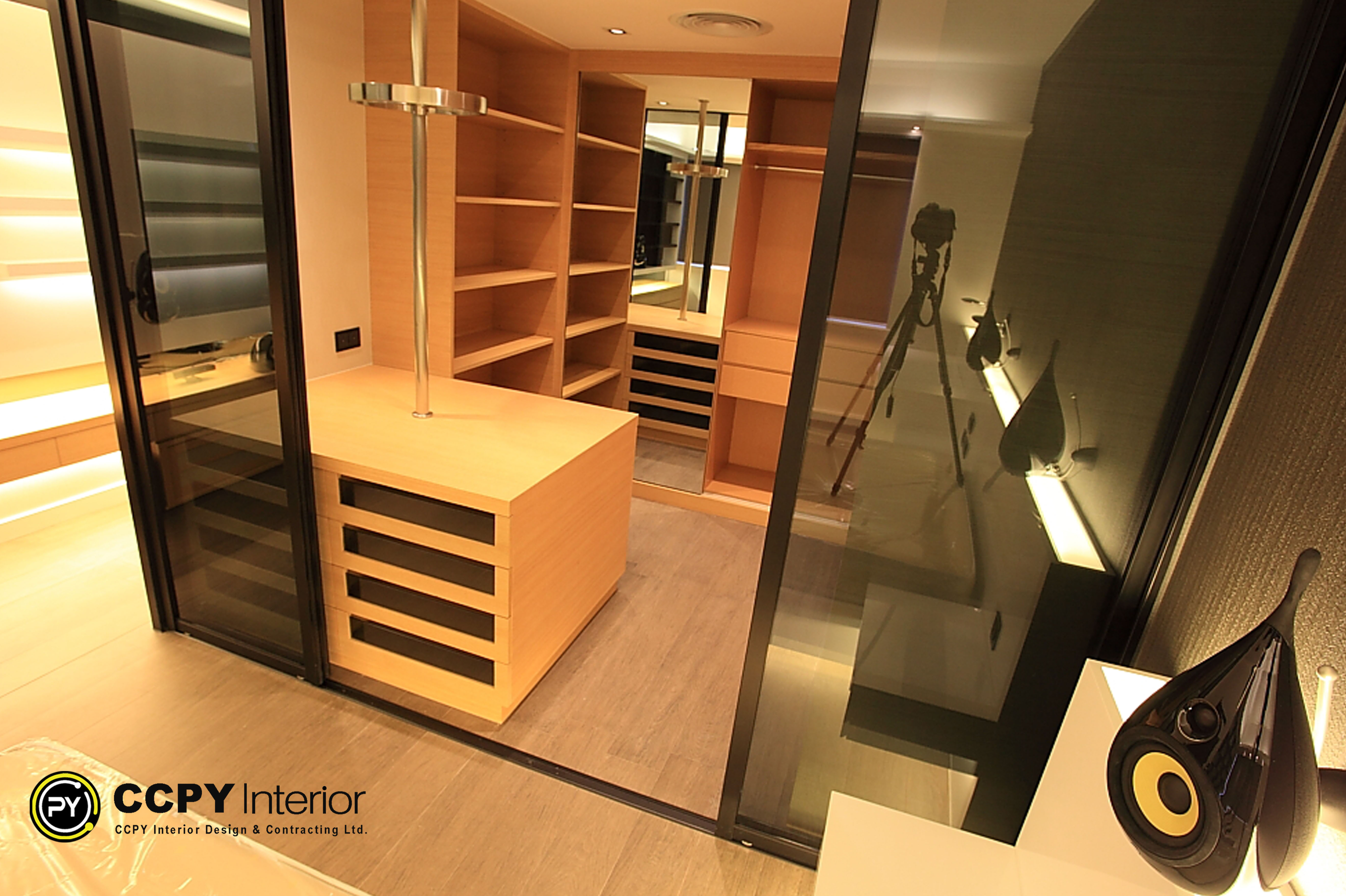 View of the glass-enclosed wardrobe at Standalone House, Perkins Road showcasing modular shelving, custom joinery, and warm integrated LED shelf lighting for visual depth.