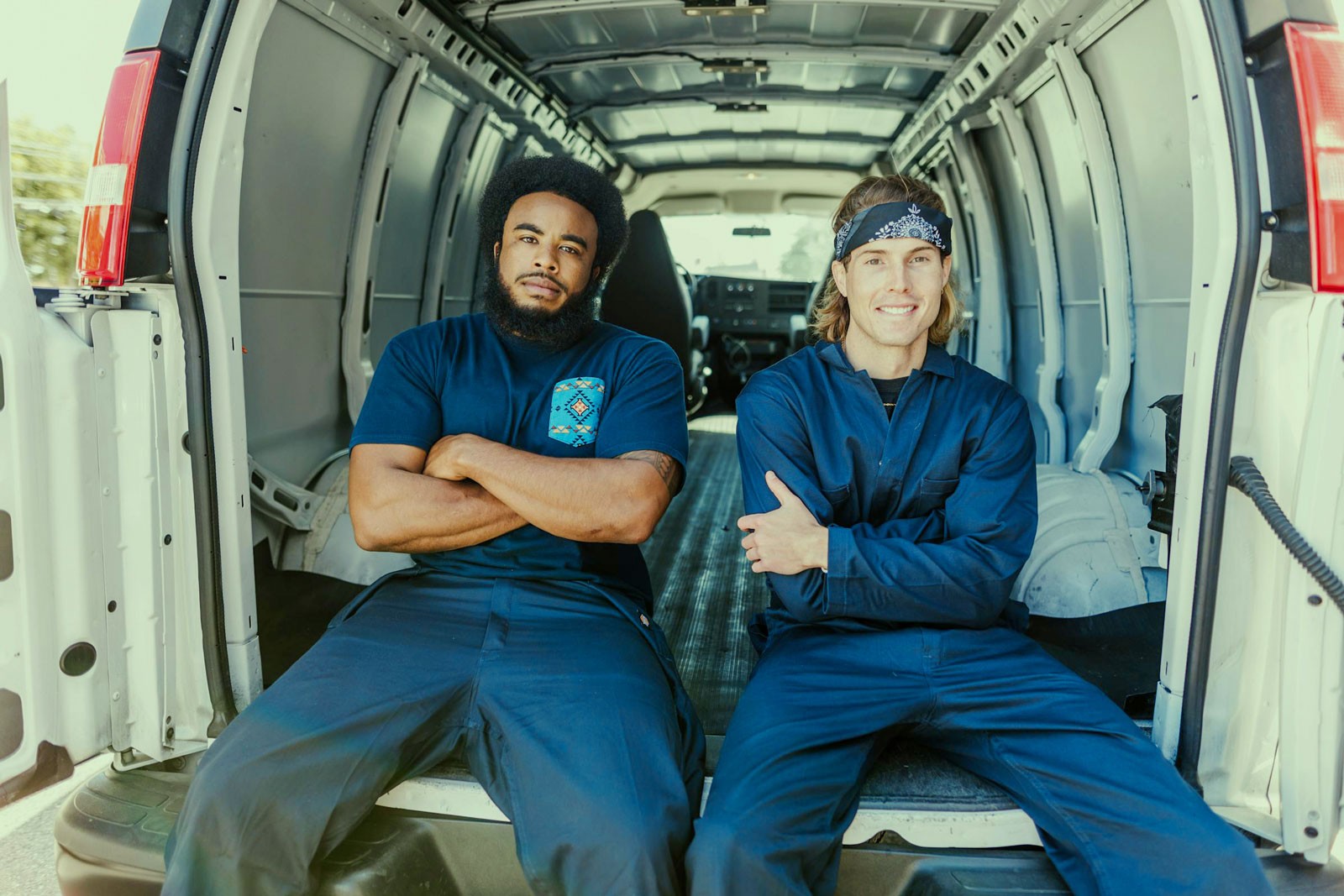 Two Moving Company workers sitted on the back of a van, smiling.