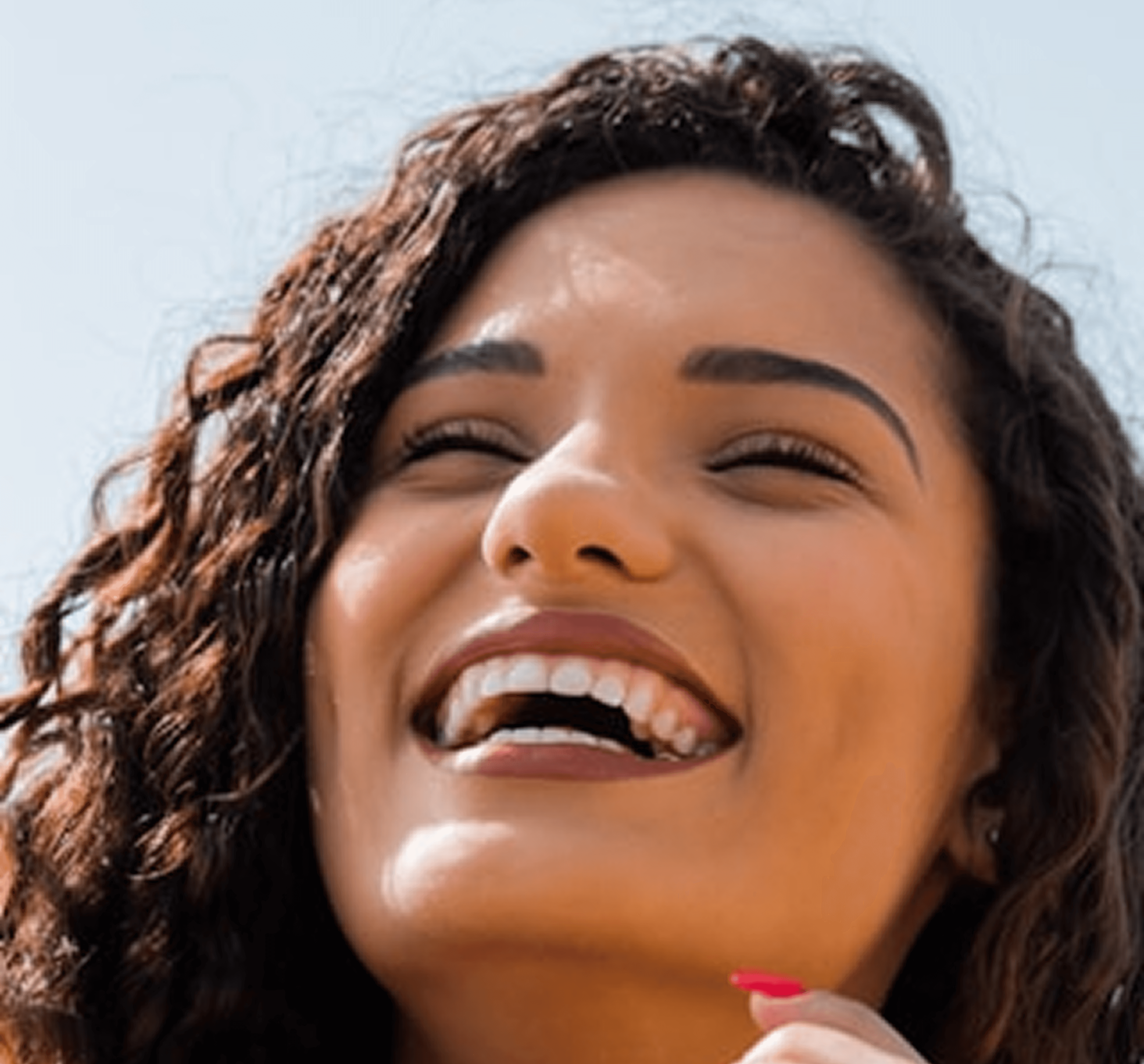 Smiling person with curly hair and closed eyes against clear sky