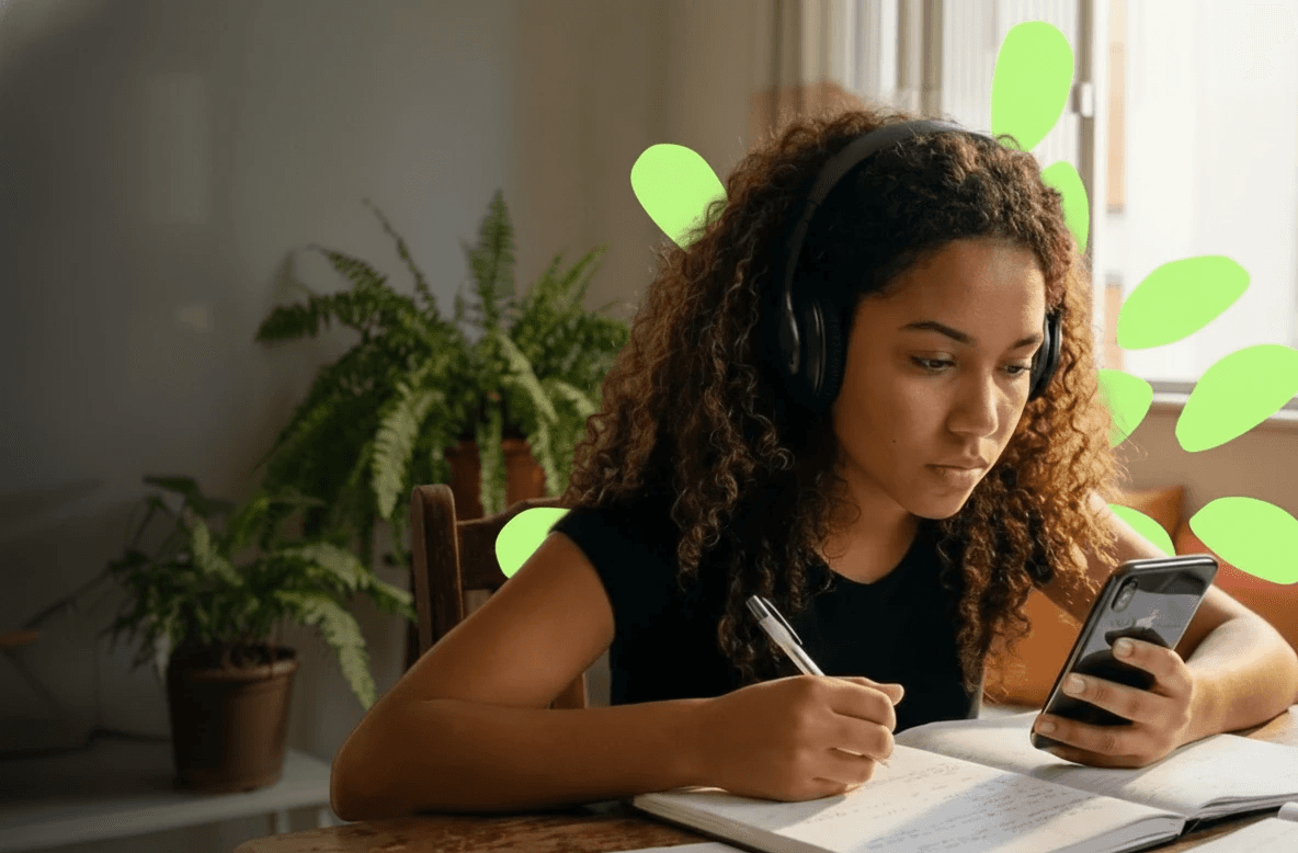 Mulher jovem estudando com um caderno e com o celular na sala de estar