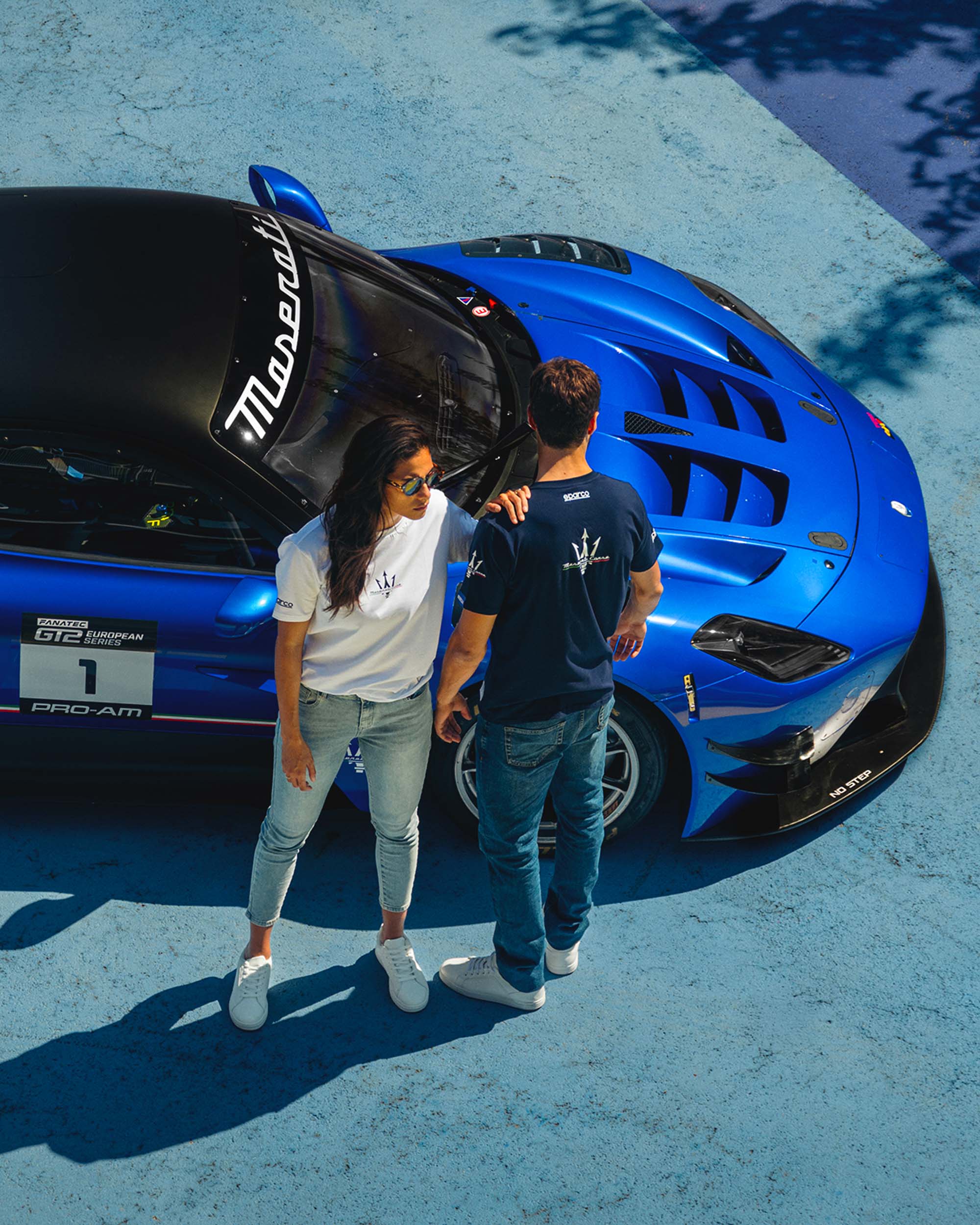 **Un homme et une femme près d’une Maserati d’endurance, vêtus de t-shirts de la marque bleu et blanc arborant le logo Maserati.**