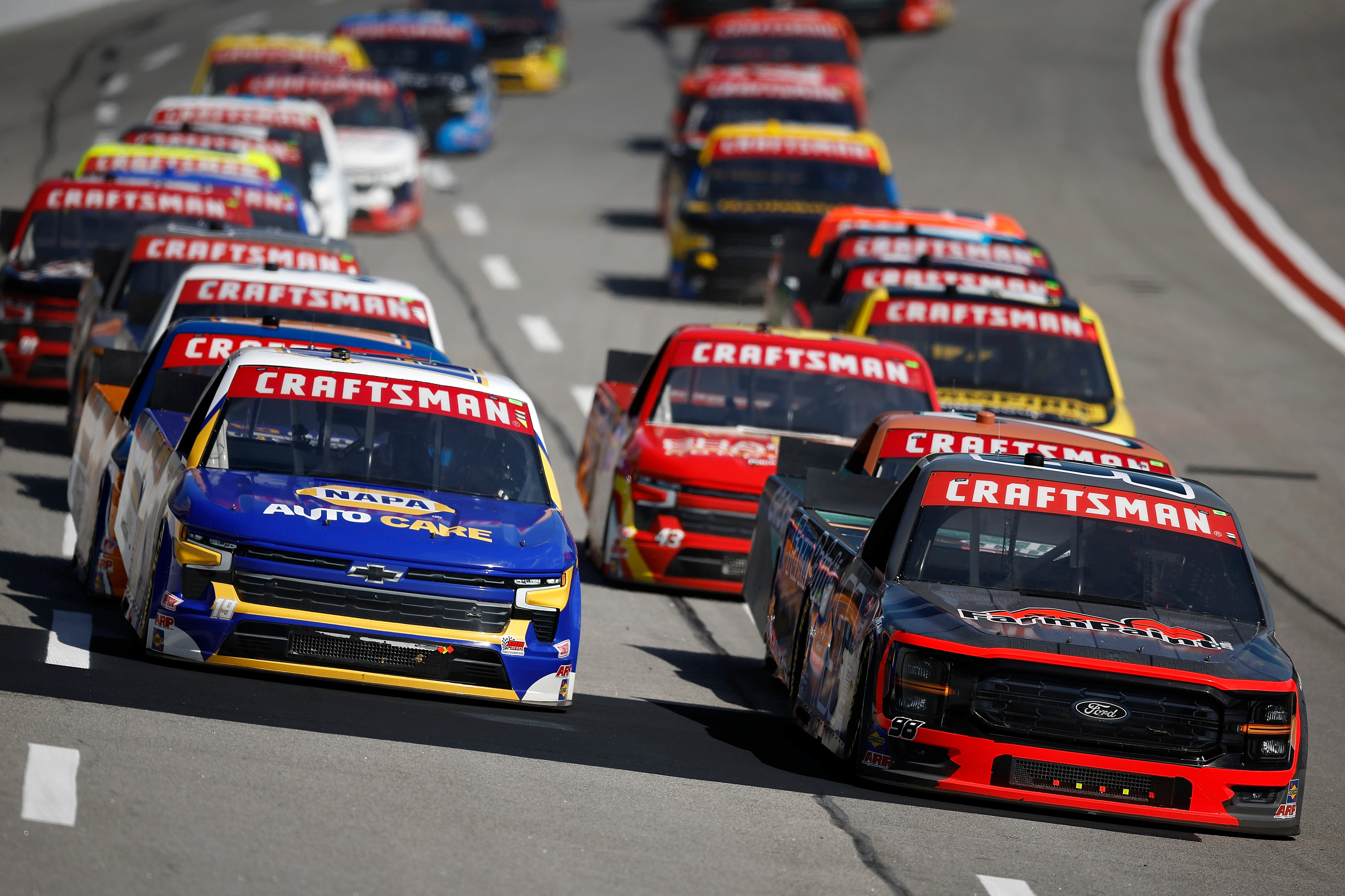 NASCAR Craftsman Truck Series drivers race tightly together during a high-intensity lap at the track.