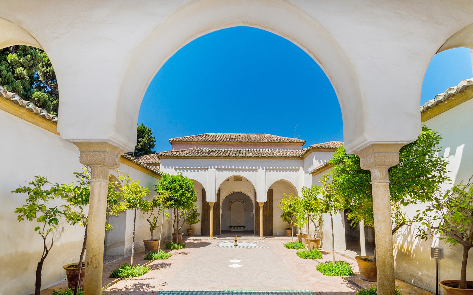 Alcazaba courtyard with arches and potted trees in Malaga, Spain.