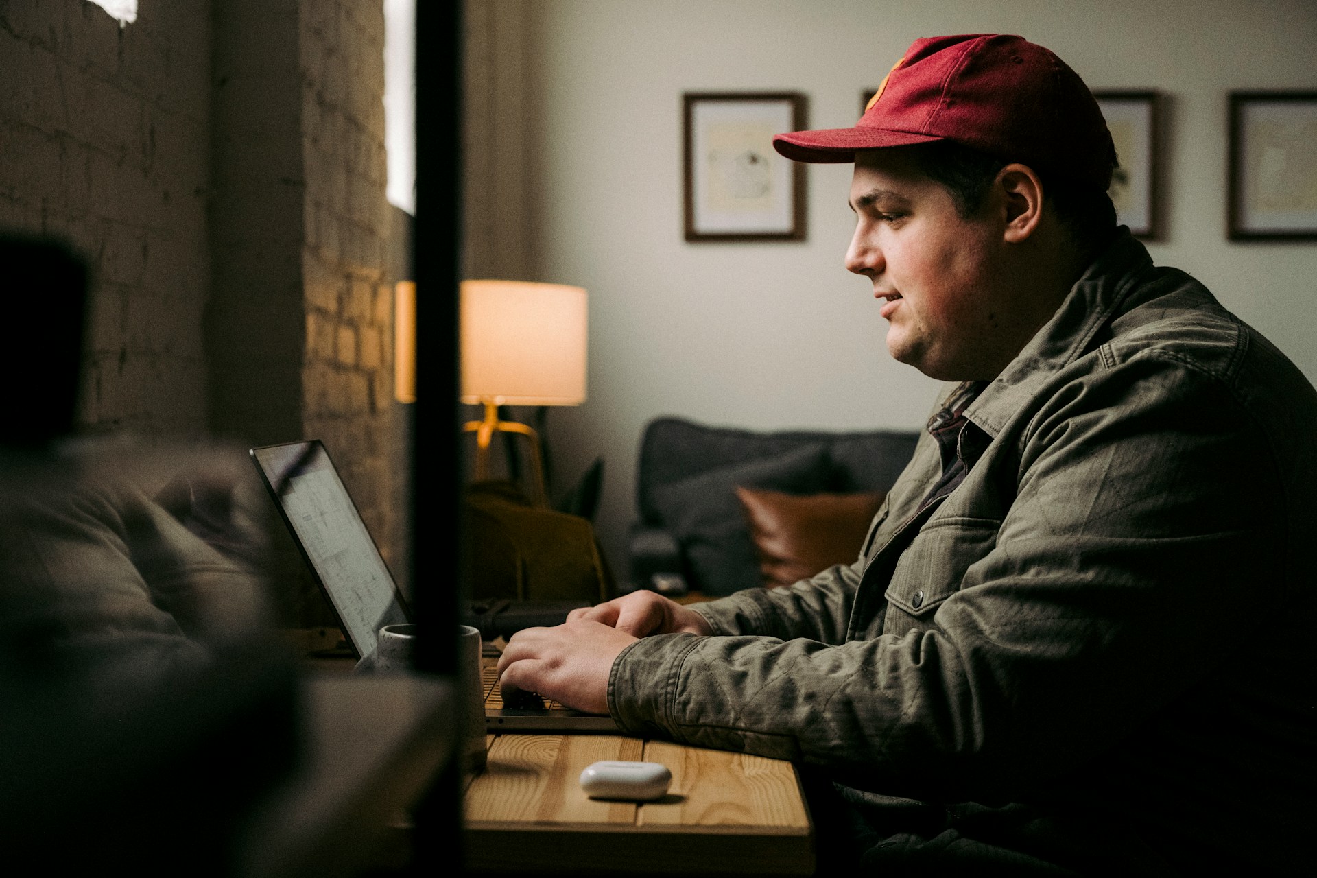 Man in a cap working on a laptop at a wooden desk