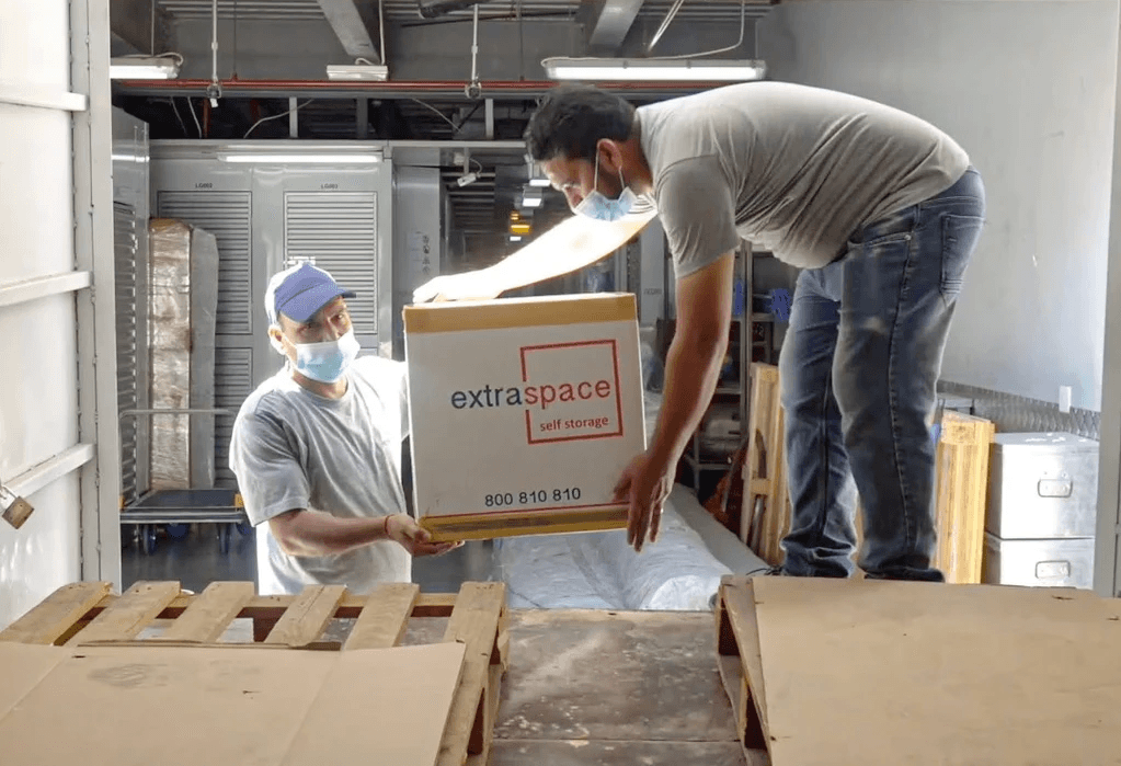 Two men in masks and gloves are loading boxes into a truck as part of an office moving operation, by Extra Space