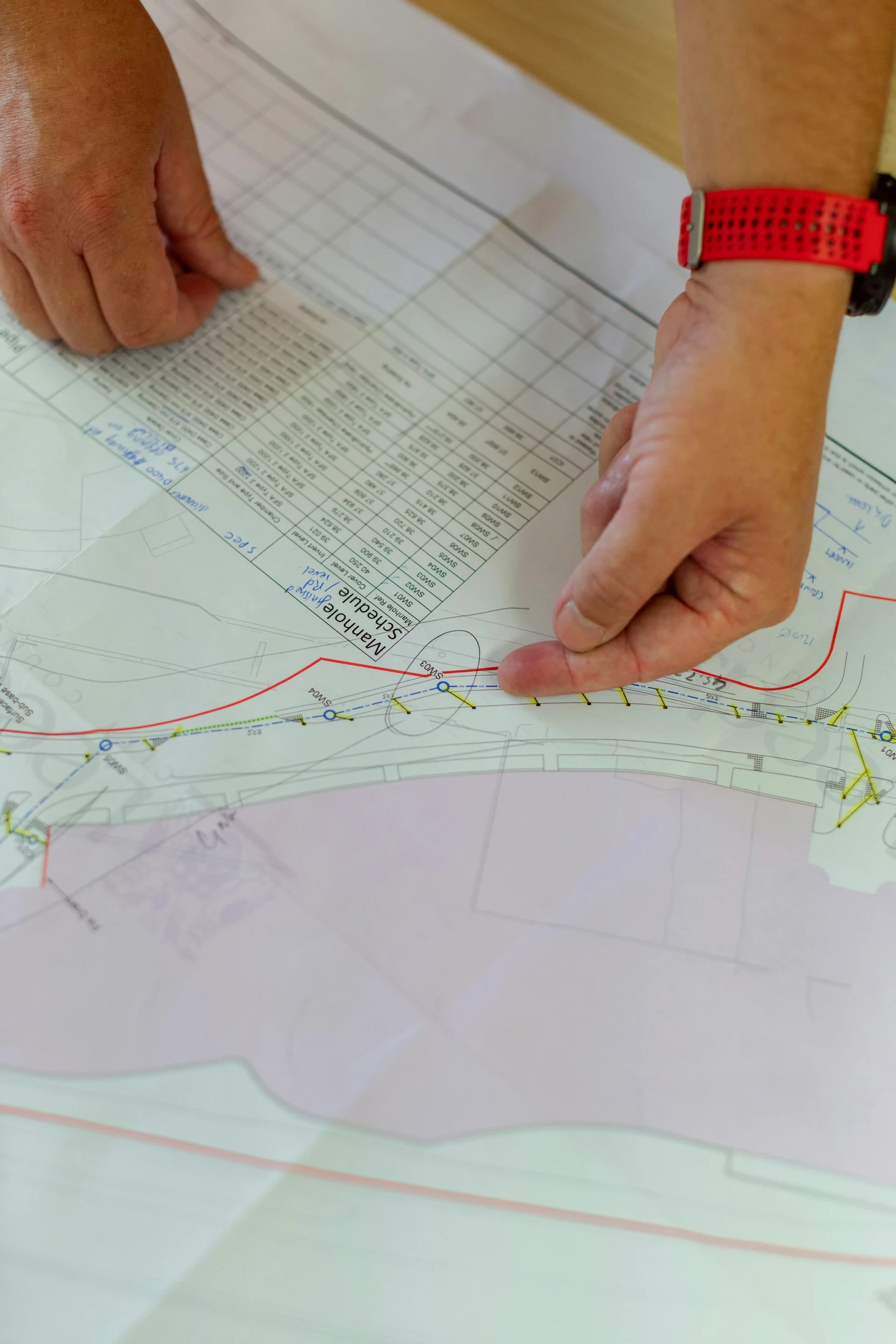 Close-up of a surveyor's hands reviewing a printed topographic survey map and manhole schedule