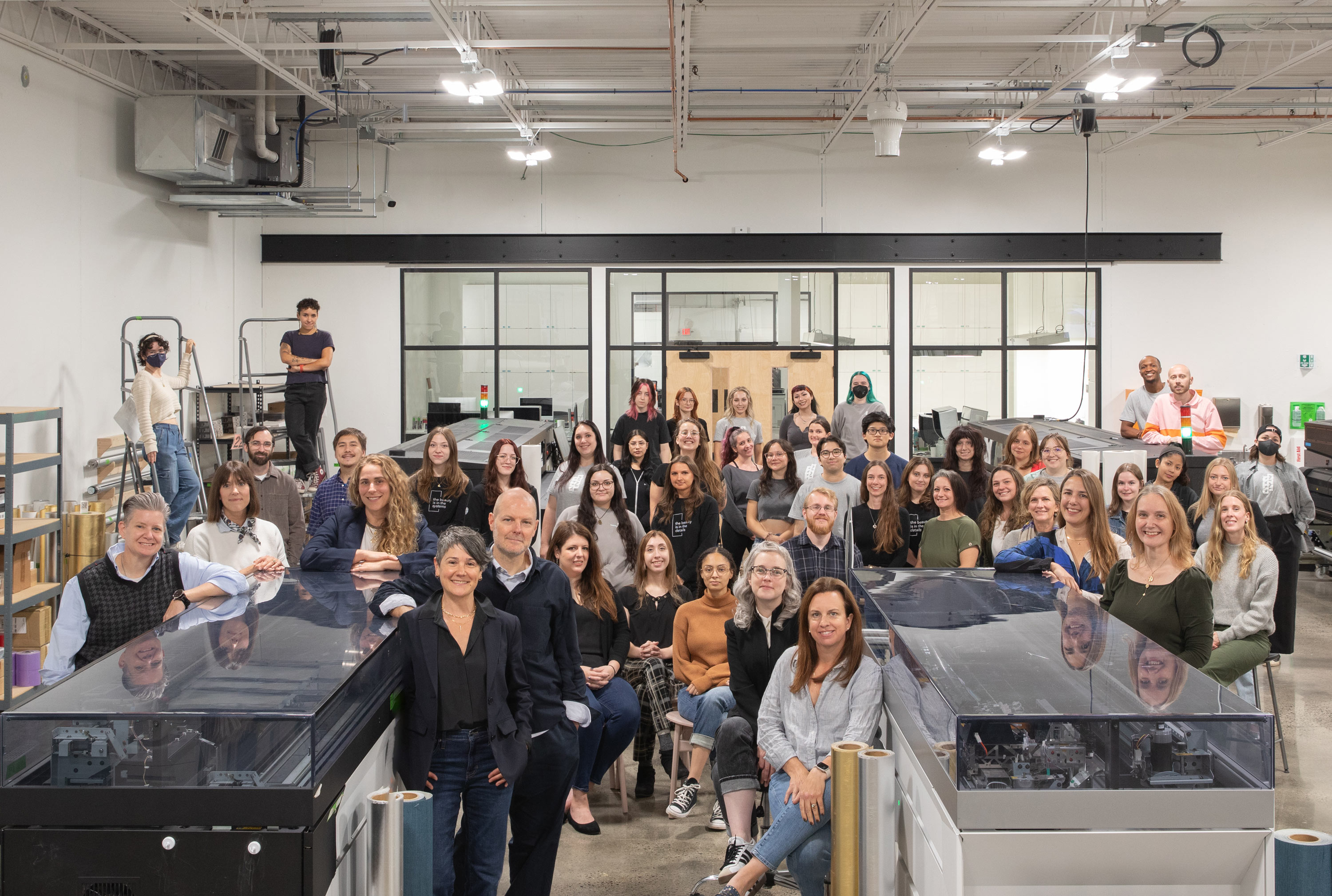 Group of smiling employees posing in front of large format printers.