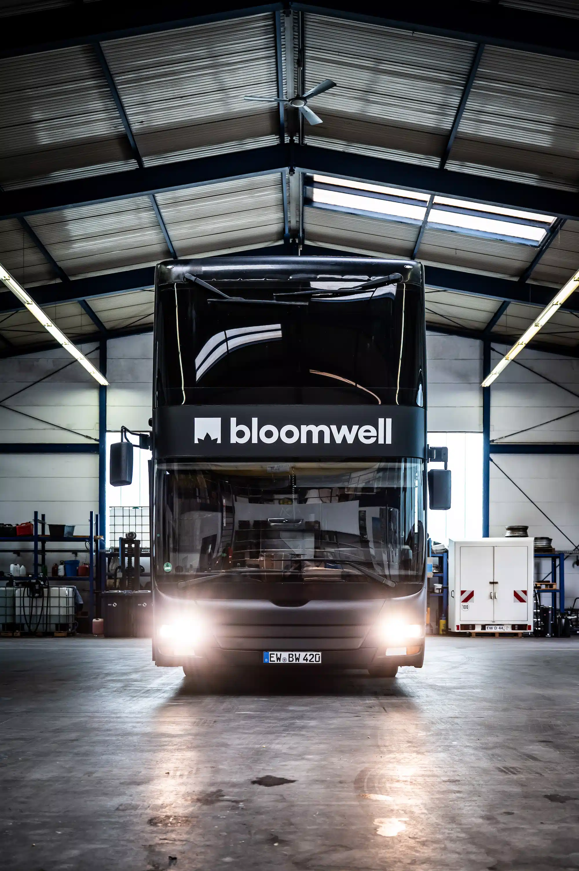 Bloomwell Cannabis App – black double-decker bus with Bloomwell branding, frontal view in a warehouse