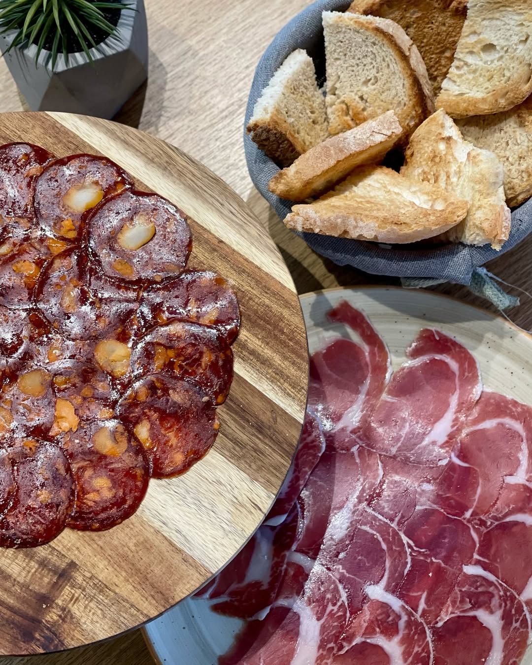 Restaurant interior with wooden tables and chairs lined against a textured wall, softly lit by round wall lamps.