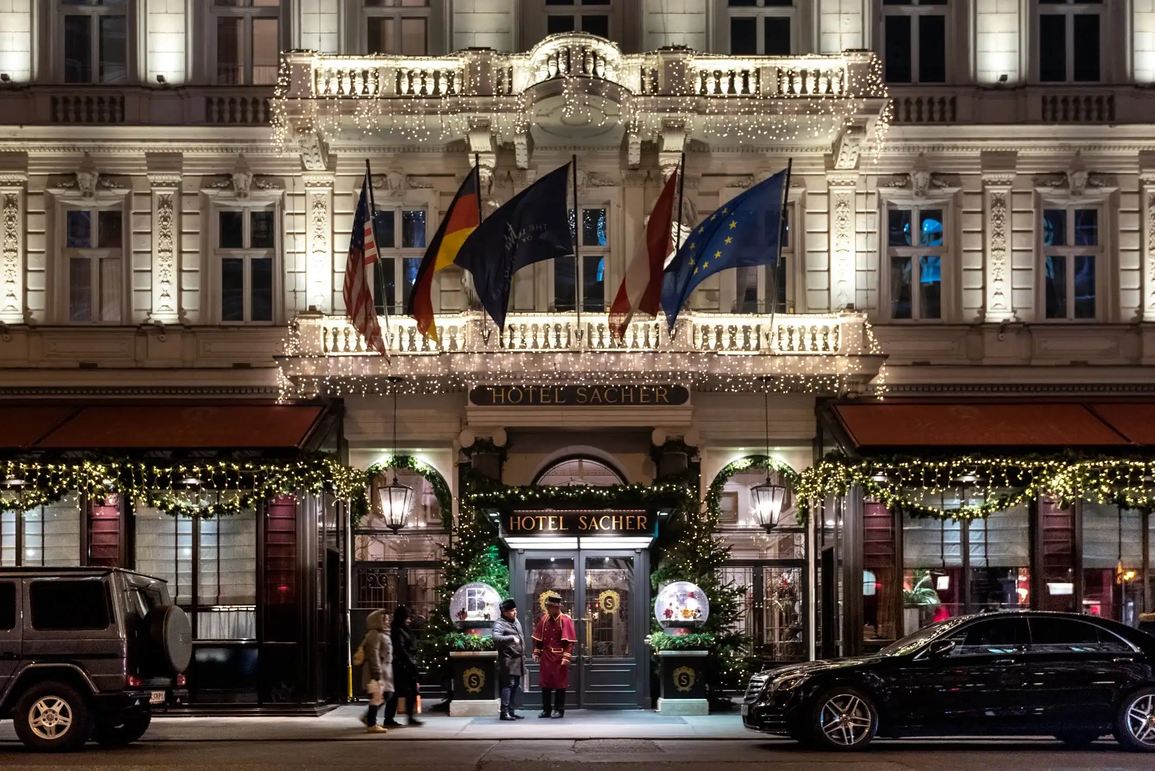 A grand theater facade with ornate gold detailing and several national flags flying above a lit entrance at night.