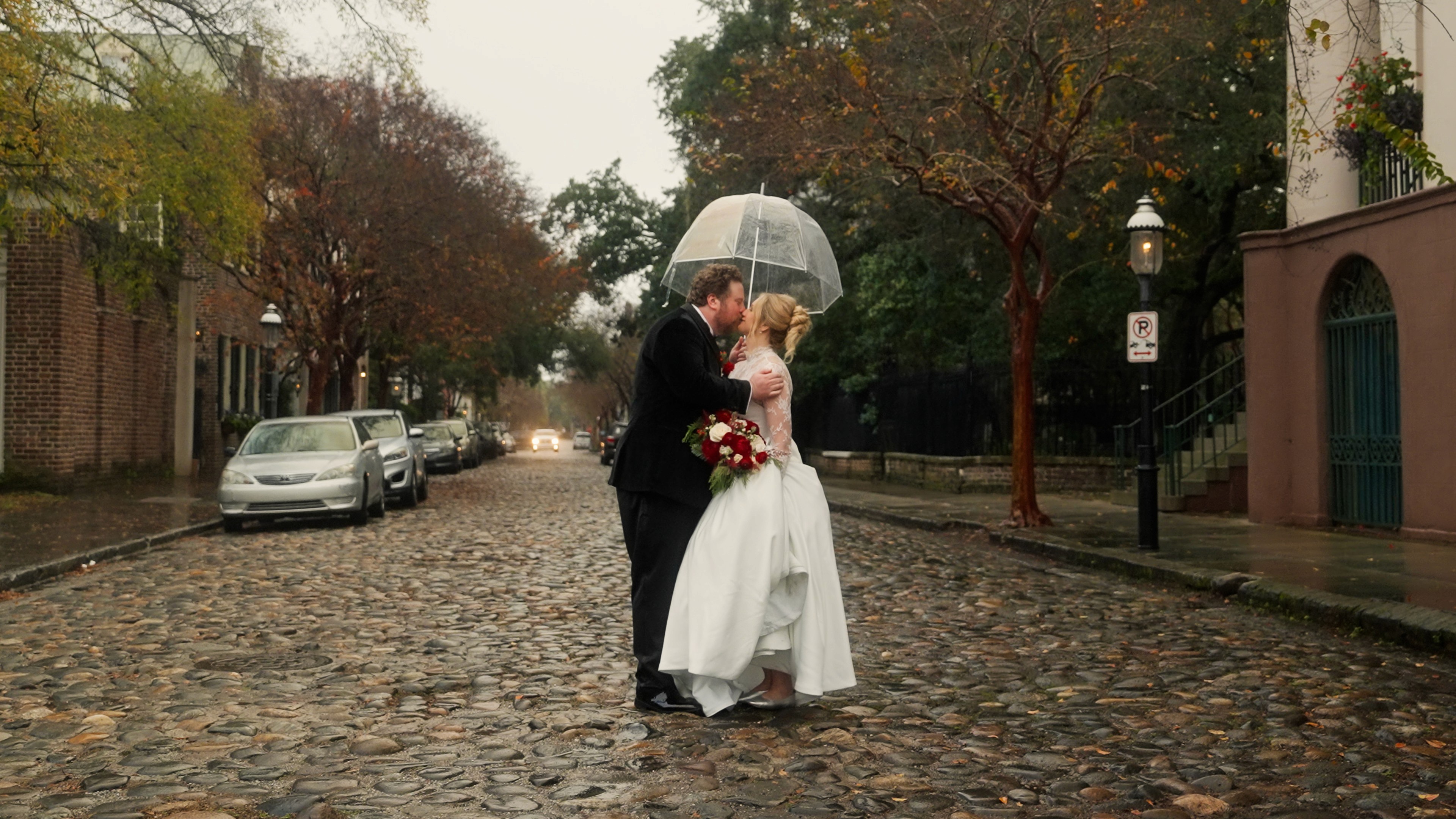 Andy and Caroline kissing beneath an umbrella on a Charleston street