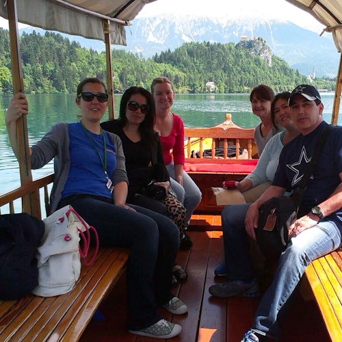 קבוצה של אנשים יושבת על סירה מעץ על אגם עם הרים ועצים ברקע.