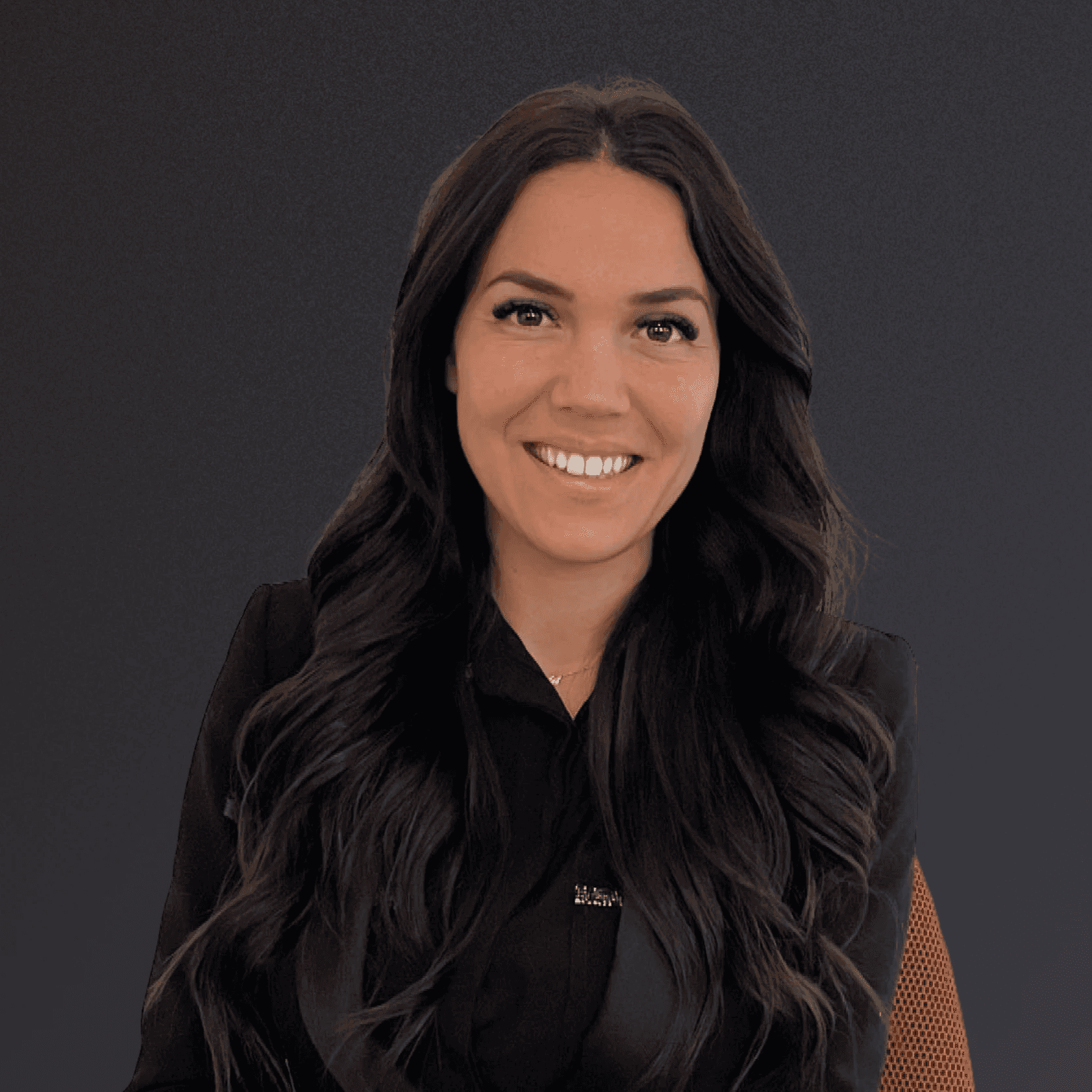 Woman with a short haircut smiling confidently, wearing a blazer and standing in warm natural light with modern architecture behind her.