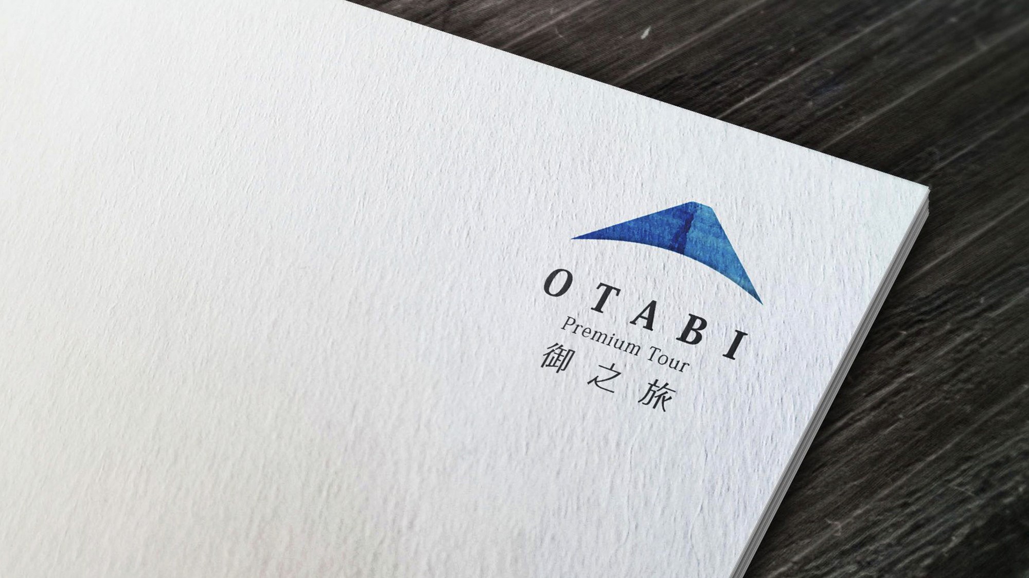 這張圖像展示了另外一款御之旅的品牌標識,有一個象徵富士山的標誌,內有漸層的藍色筆刷感,標誌底下寫有「OTABI Premium Tour」和「御之旅」的字。