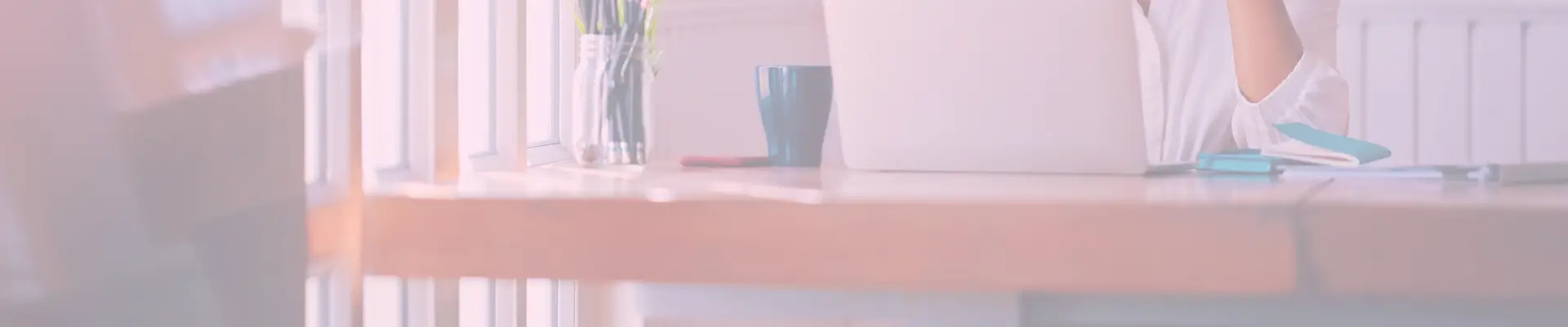 Bright, sun-drenched desk scene with a mug, open laptop, and glass jar of pencils in a cozy workspace.