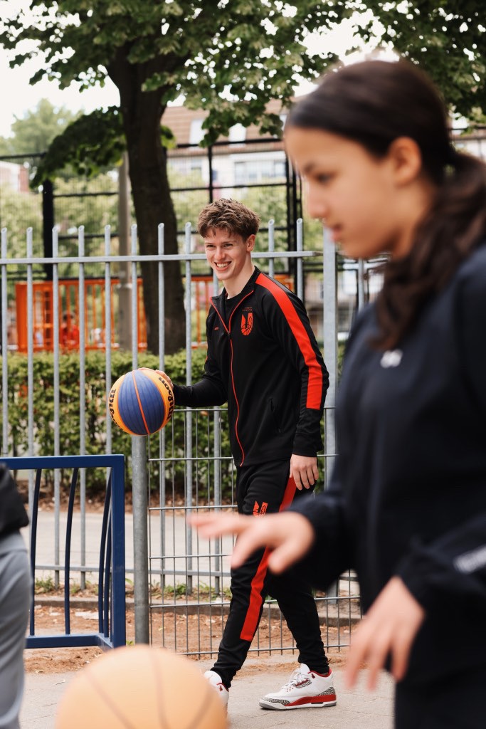 A dimly lit gym scene featuring a barbell rack and weights on the floor, with large windows in the background.