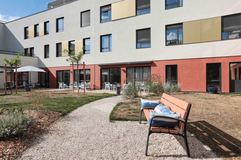 Residential courtyard with paved area, outdoor seating, modern multi-story building with red and white facade