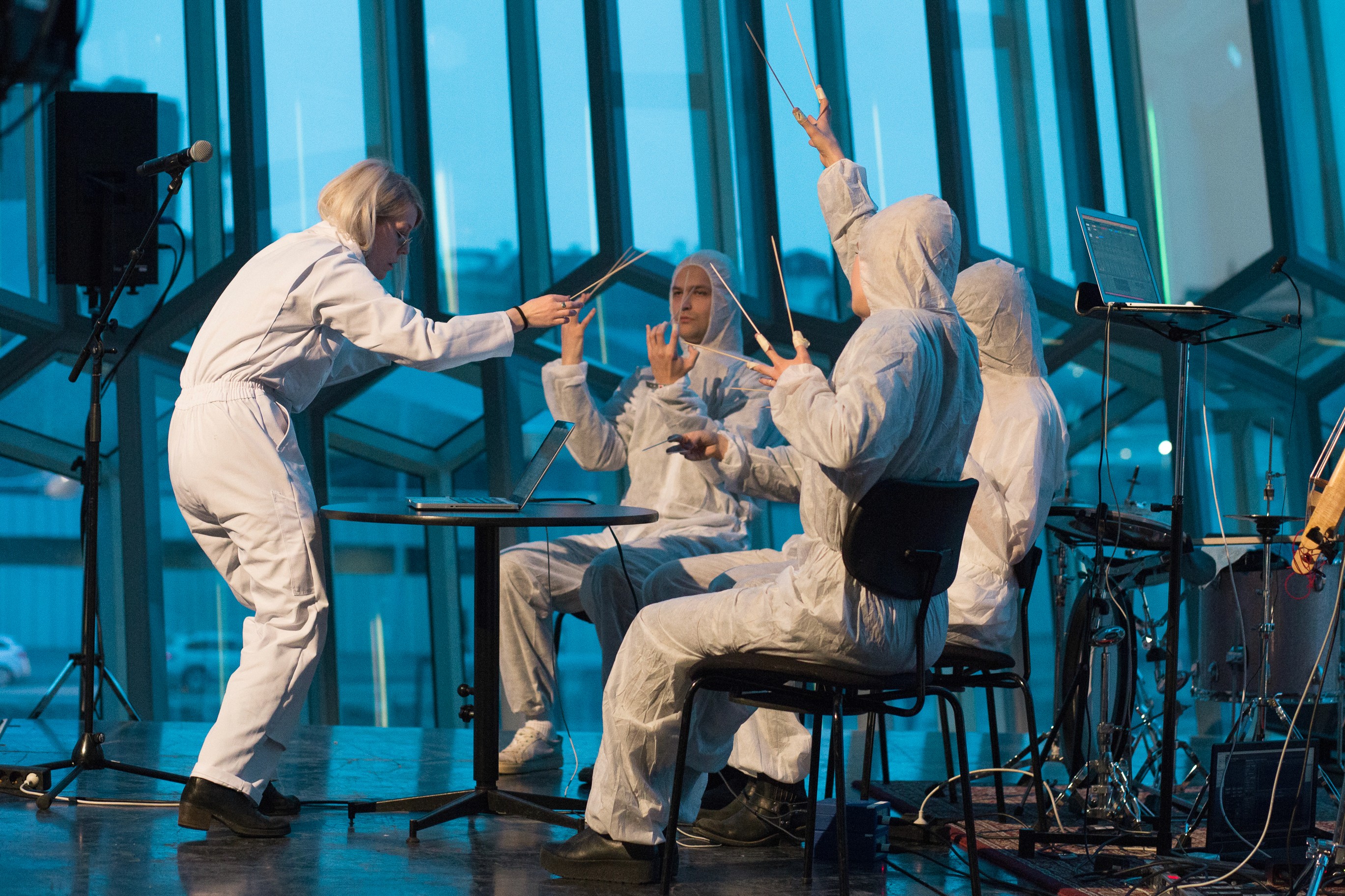 A performance still from The Concert by Ásta Fanney Sigurðardóttir, with four performers in white coveralls holding thin batons inside Reykjavík's Harpa concert hall.