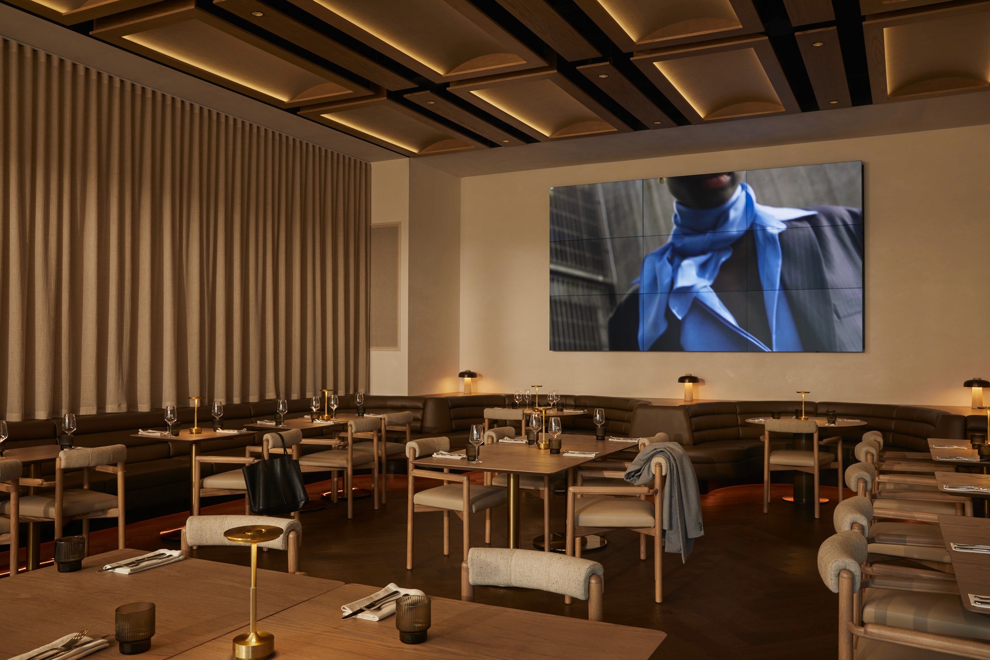Empty restaurant dining room set for service with a video wall showing a man in a scarf and blazer