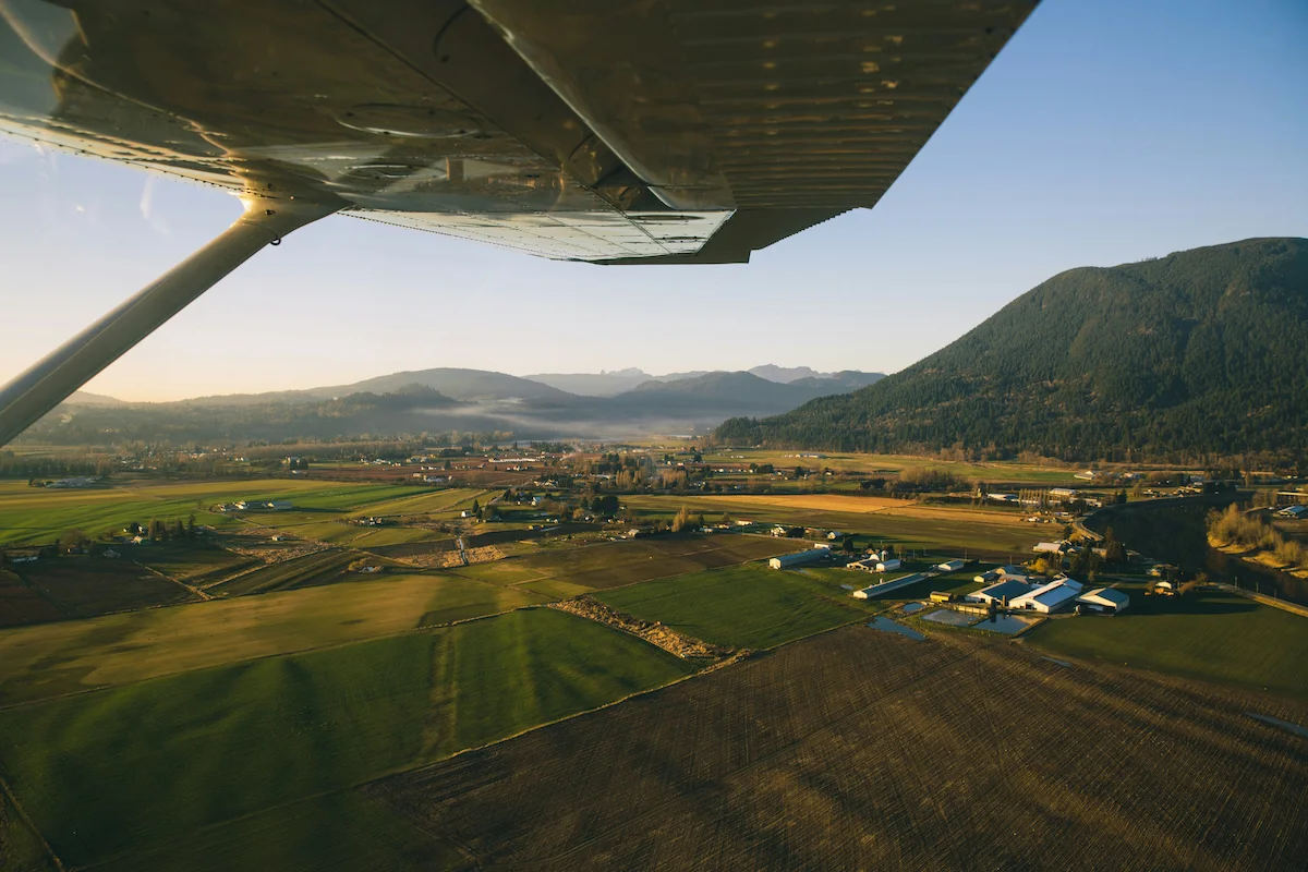 Aerial view of farmland in Langley, BC, with fields, farm buildings, and mountain ranges in the distance at sunrise.