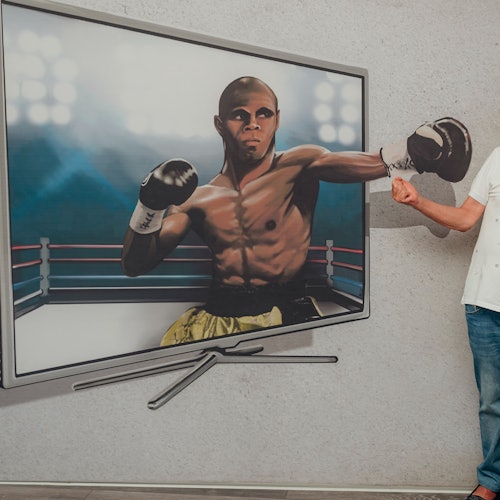 A man in jeans and a white shirt stands next to a painting of a boxer, appearing to punch into the boxer's extended glove.