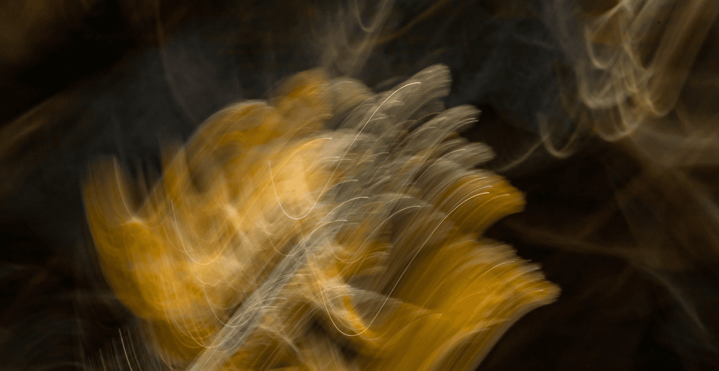 Abstract motion-blurred light patterns in warm gold and green tones against a dark background.