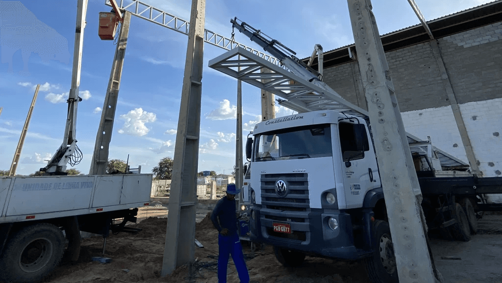 Montagem de estrutura metálica em obra, com guindaste e caminhão plataforma auxiliando na elevação de vigas de concreto