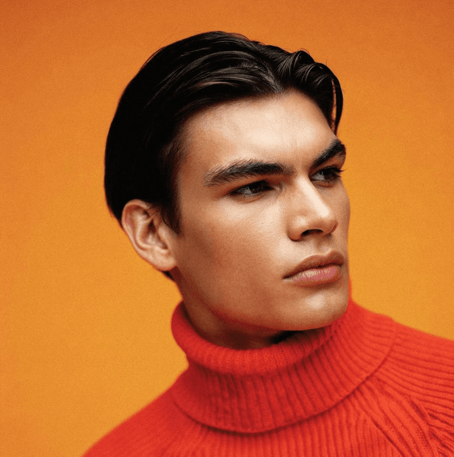 Young man in a vibrant orange turtleneck against a matching orange background, gazing thoughtfully to the right, creating a striking, cohesive look.
