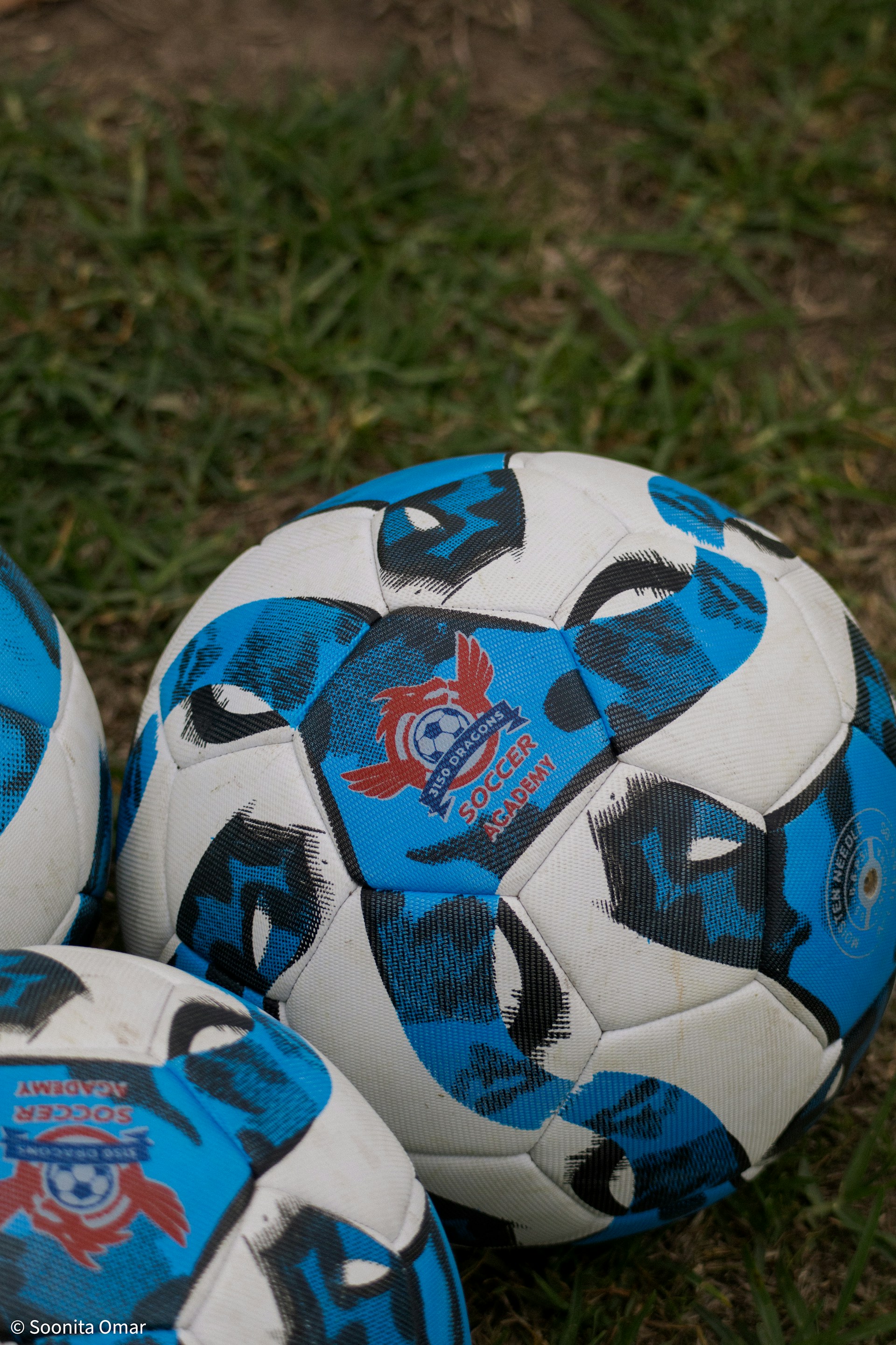 A close-up view of several blue and white soccer balls with red logos resting on green grass.