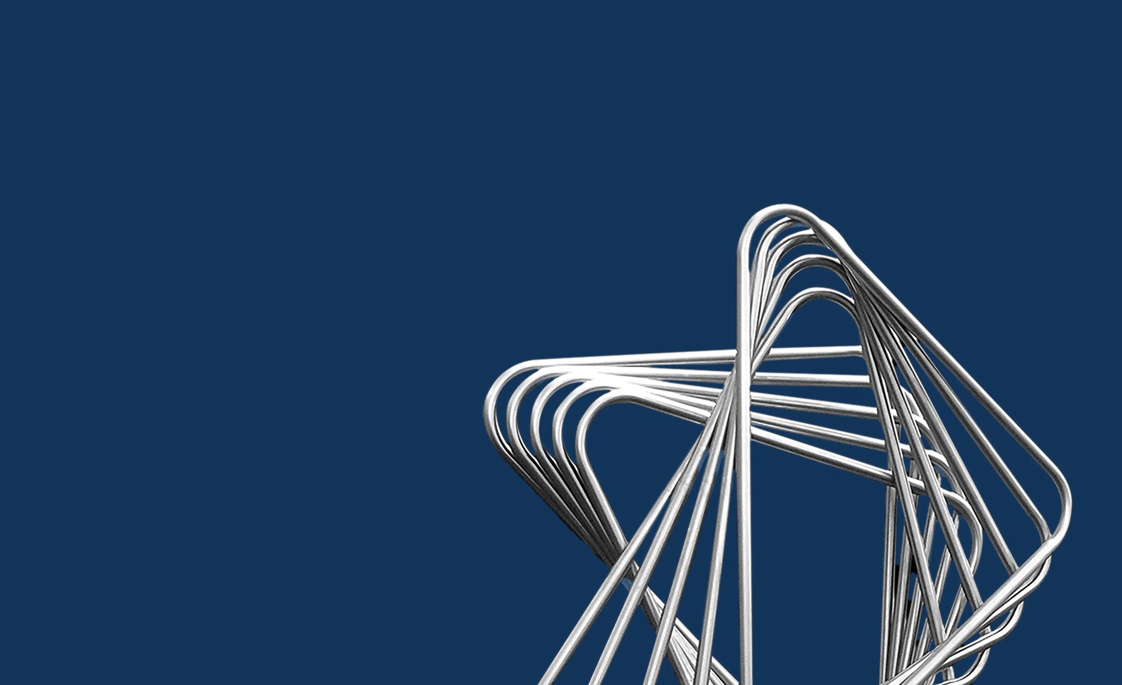 A shiny, abstract silver sculpture with curved loops set against a solid dark blue background, creating a modern and minimalist aesthetic.