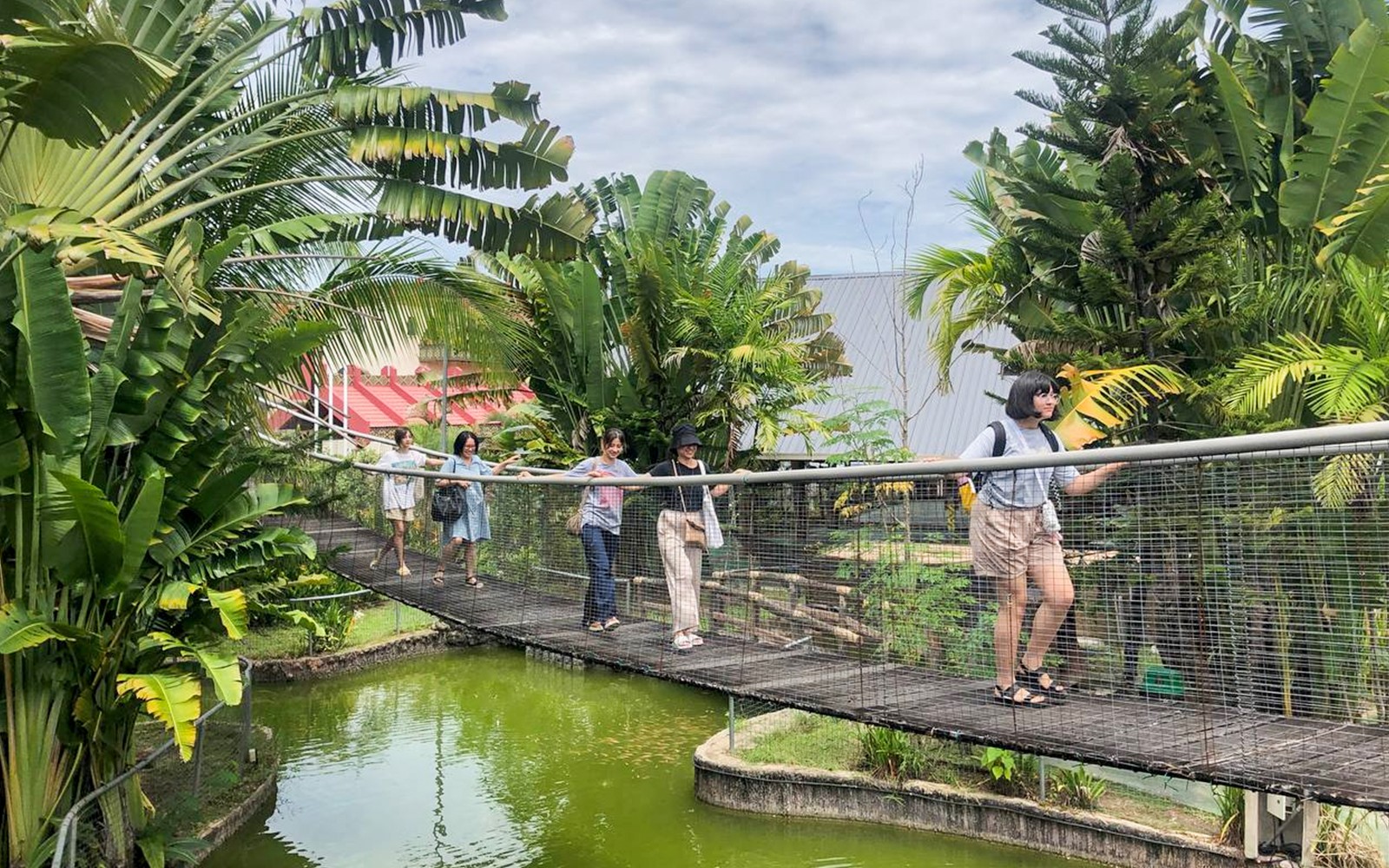 Visitors walking on a bridge at Koisaan Cultural Village, surrounded by lush greenery.