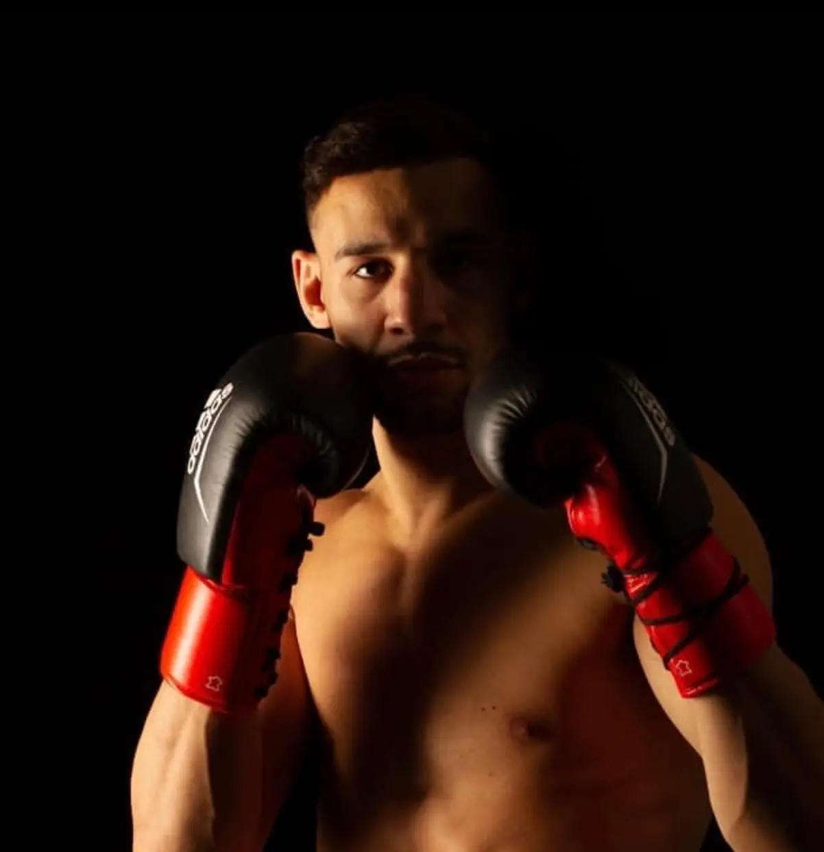 Ismail Airoud posing with red boxing gloves in a dark-lit environment — boxing specialist at The Alpha Club.