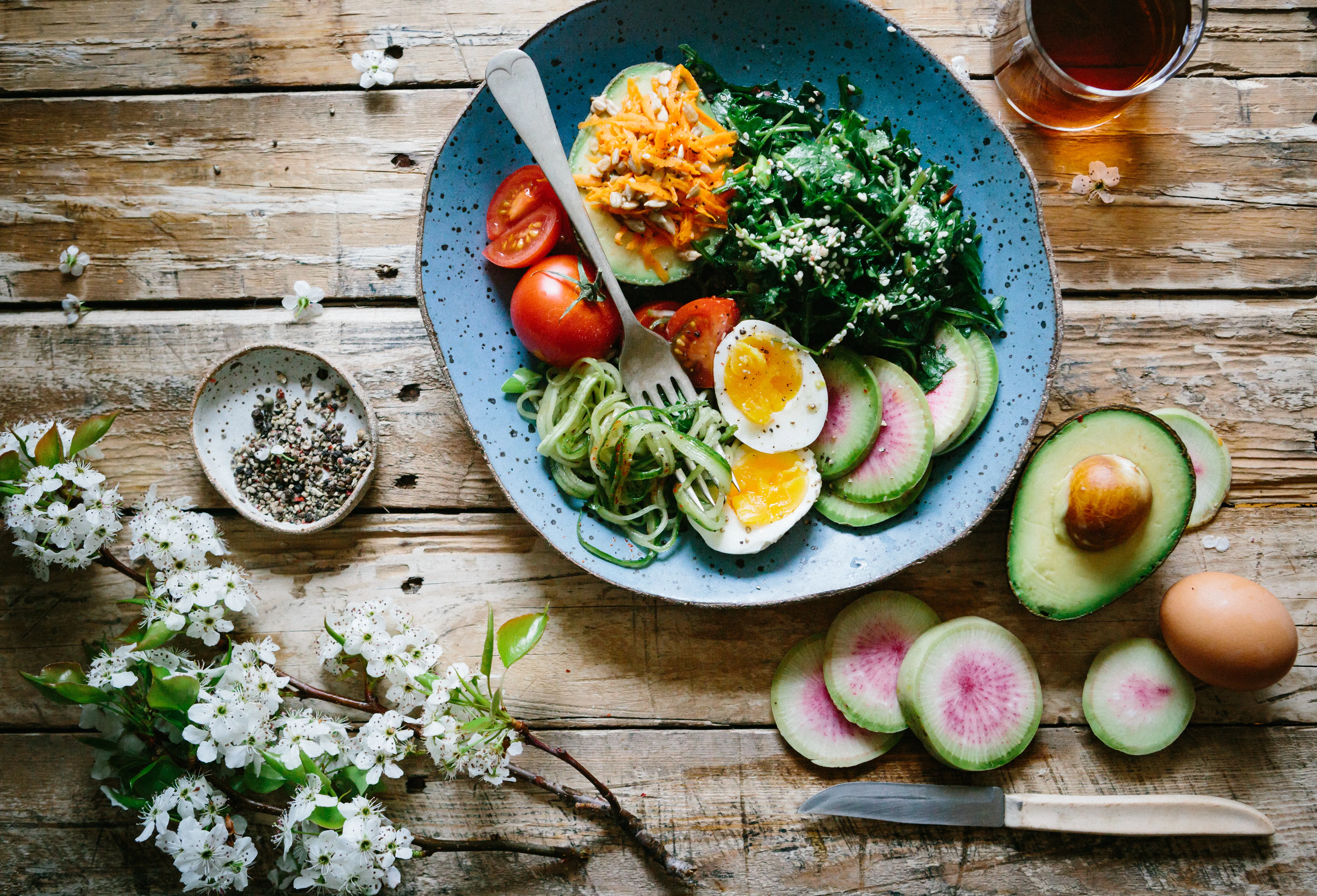 Colorful plate of healthy food including eggs, avocado, greens, tomatoes, and sliced radish on a rustic wooden table.