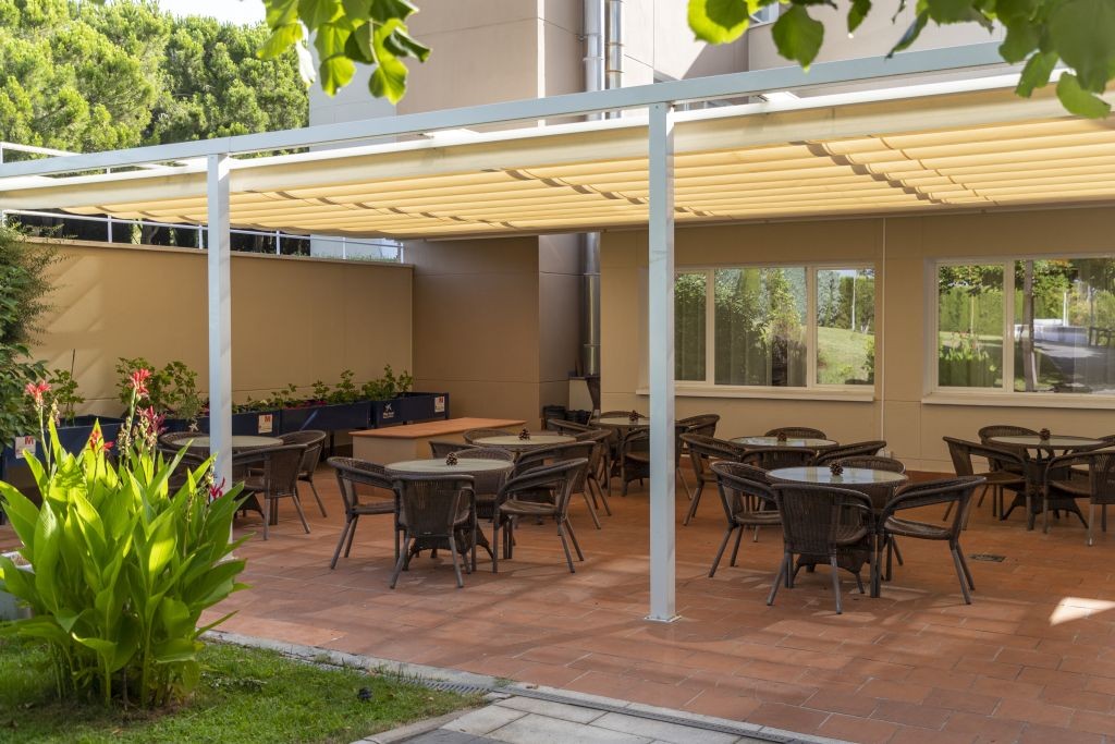 Shaded outdoor terrace with wicker furniture surrounded by greenery.