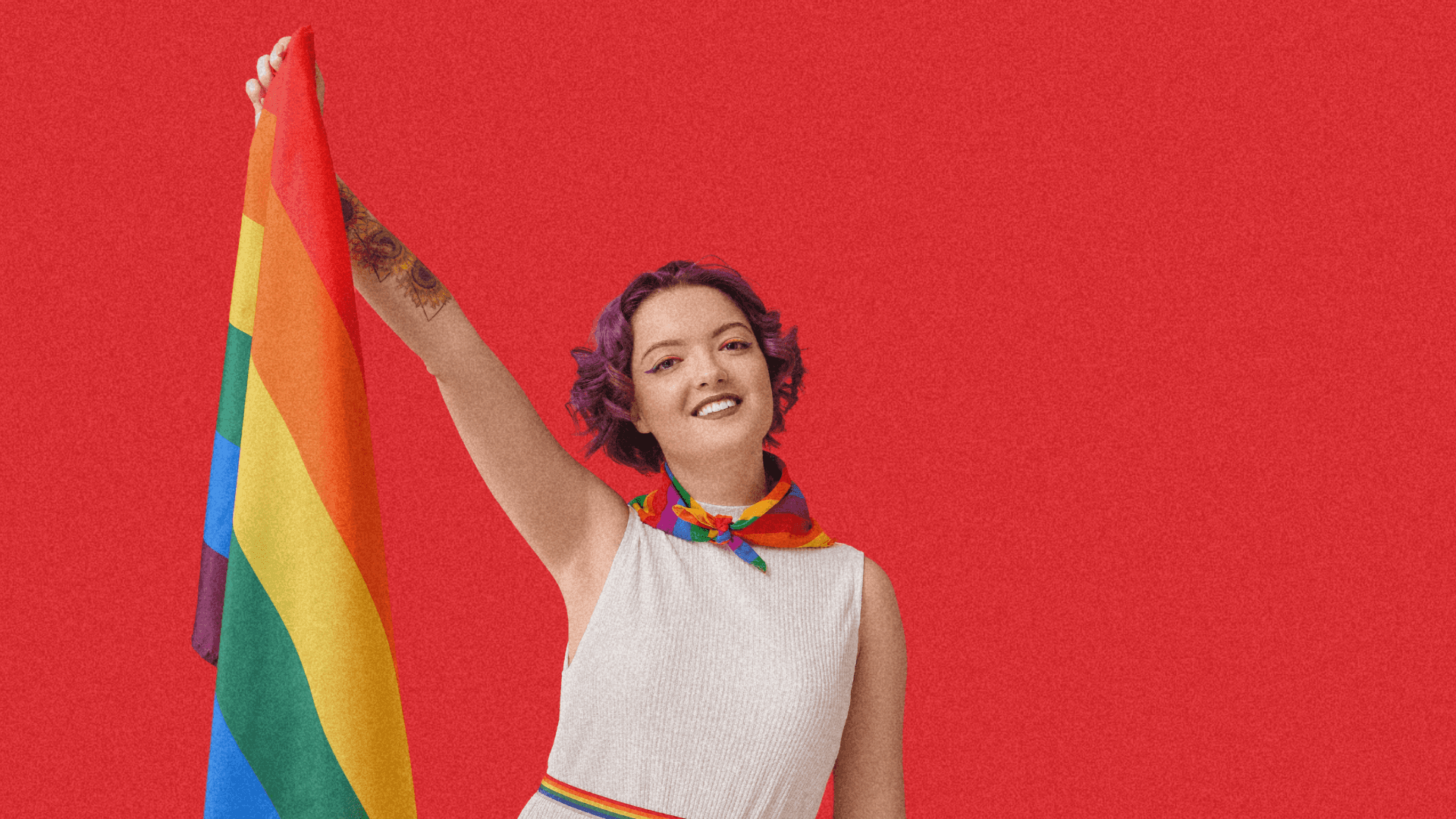 A person smiles and raises a rainbow flag against a red background, celebrating LGBTQ+ pride.