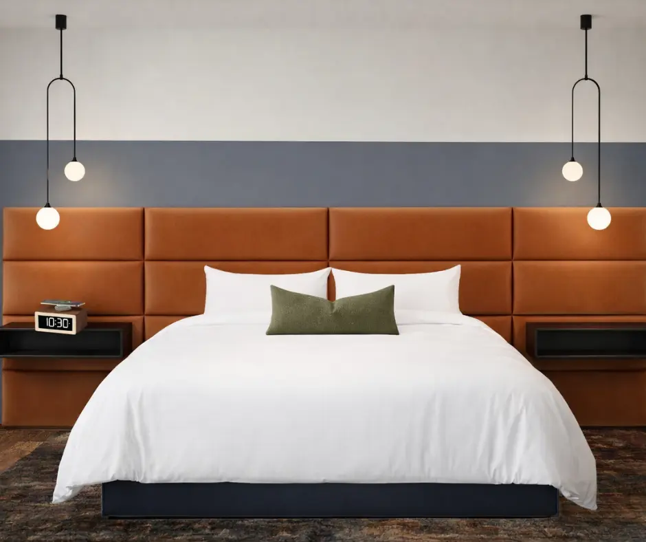 A stylish bedroom featuring a large bed with white linens, a green accent pillow, and modern pendant lighting.