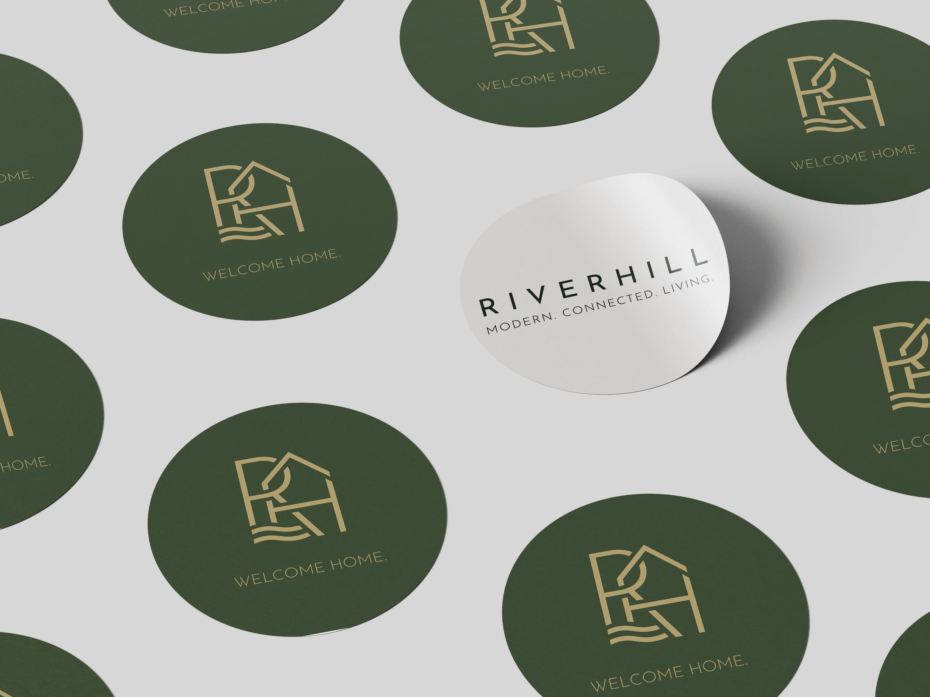 Graphic design mockup of a group of stickers for the Riverhill housing community — modern, geometric brandmark logo integrating the brand name initials, a house, and a river with a clean sans serif typography, designed by Will Lefkovich.