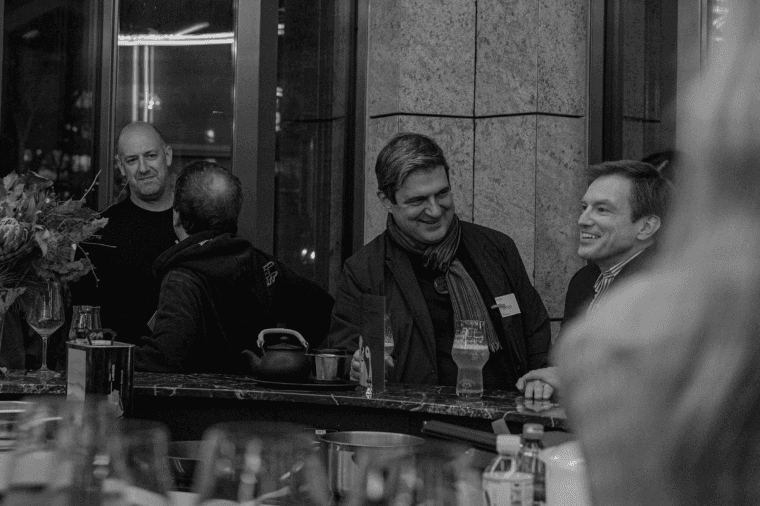 A group of individuals gathered around a bar, engaged in animated discussion. This setting reflects collective strategizing, emphasizing the importance of diverse perspectives in crafting effective strategies.