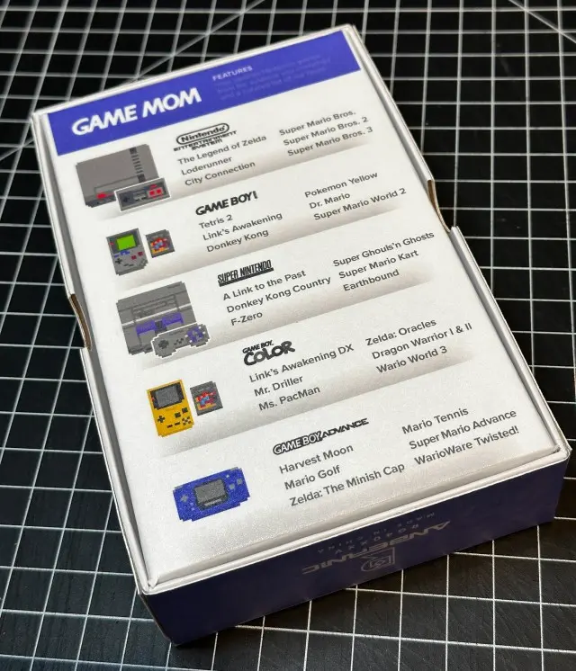 The image shows a boxed set called "Game Mom" featuring a curated collection of classic gaming consoles including versions similar to Nintendo Entertainment System, Game Boy, Game Boy Color, and Game Boy Advance, displayed with a list of iconic games for each console on a black grid background, possibly designed by Rob Harrigan.