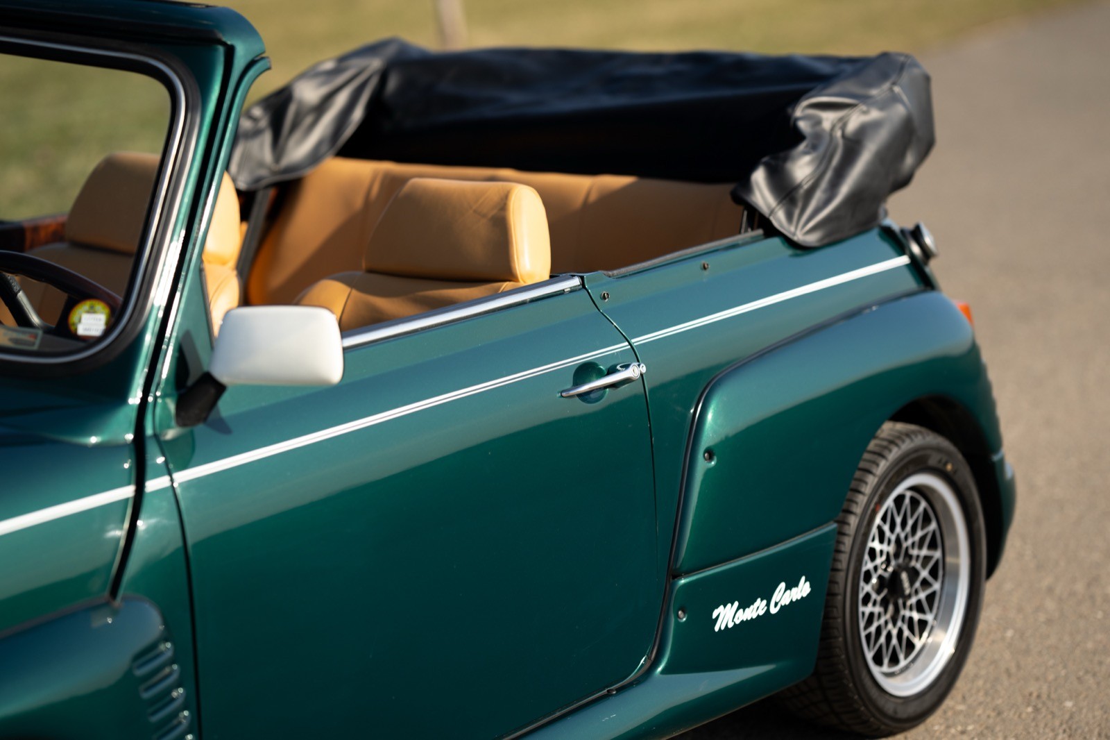 A close-up of a green convertible car with the top down, revealing a tan interior, parked outdoors.